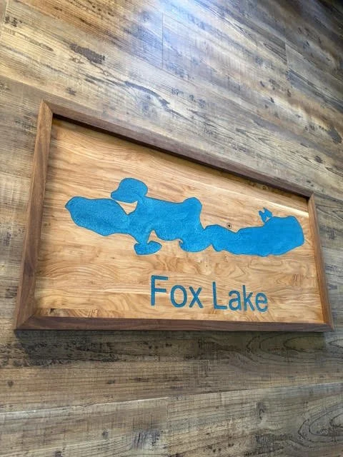 Angled view of a custom Fox Lake wooden sign with a bright blue lake map inlay and natural hardwood frame.