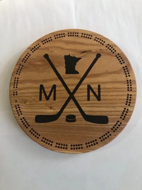 Round wooden cribbage board featuring crossed hockey sticks, a puck, and a Minnesota state silhouette with engraved MN lettering.