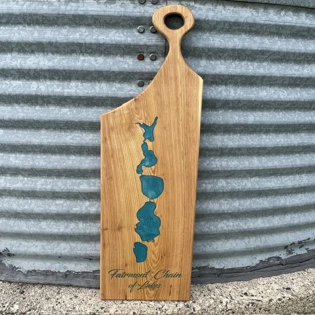 Handcrafted wooden serving board featuring blue inlays of the Fairmont Chain of Lakes, engraved lettering, and a rounded handle.