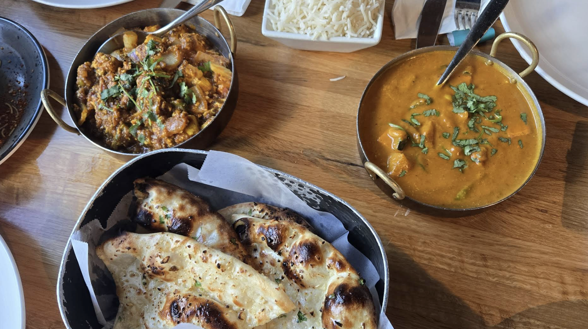Indian meal with naan bread, curry, and vegetable dishes on a wooden table.