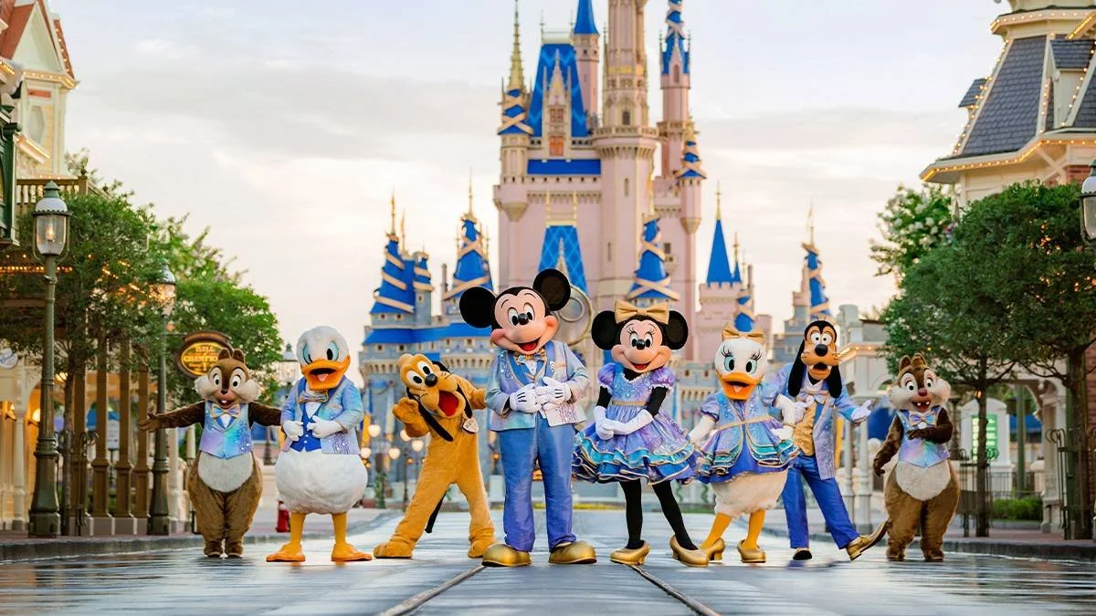 Disney characters Mickey Mouse, Minnie Mouse, Donald Duck, Goofy, Daisy Duck, and Chip and Dale in costumes, standing on Main Street at Disneyland in front of Sleeping Beauty Castle.