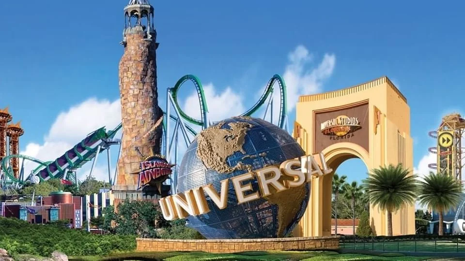 The Universal Studios globe at a theme park entrance with roller coasters and a tall tower in the background.