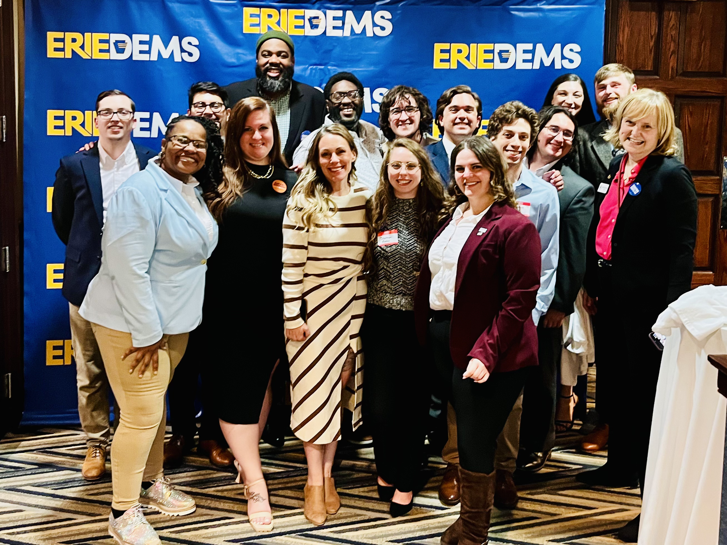Photo of a group of young people smiling in front of an ErieDems banner.