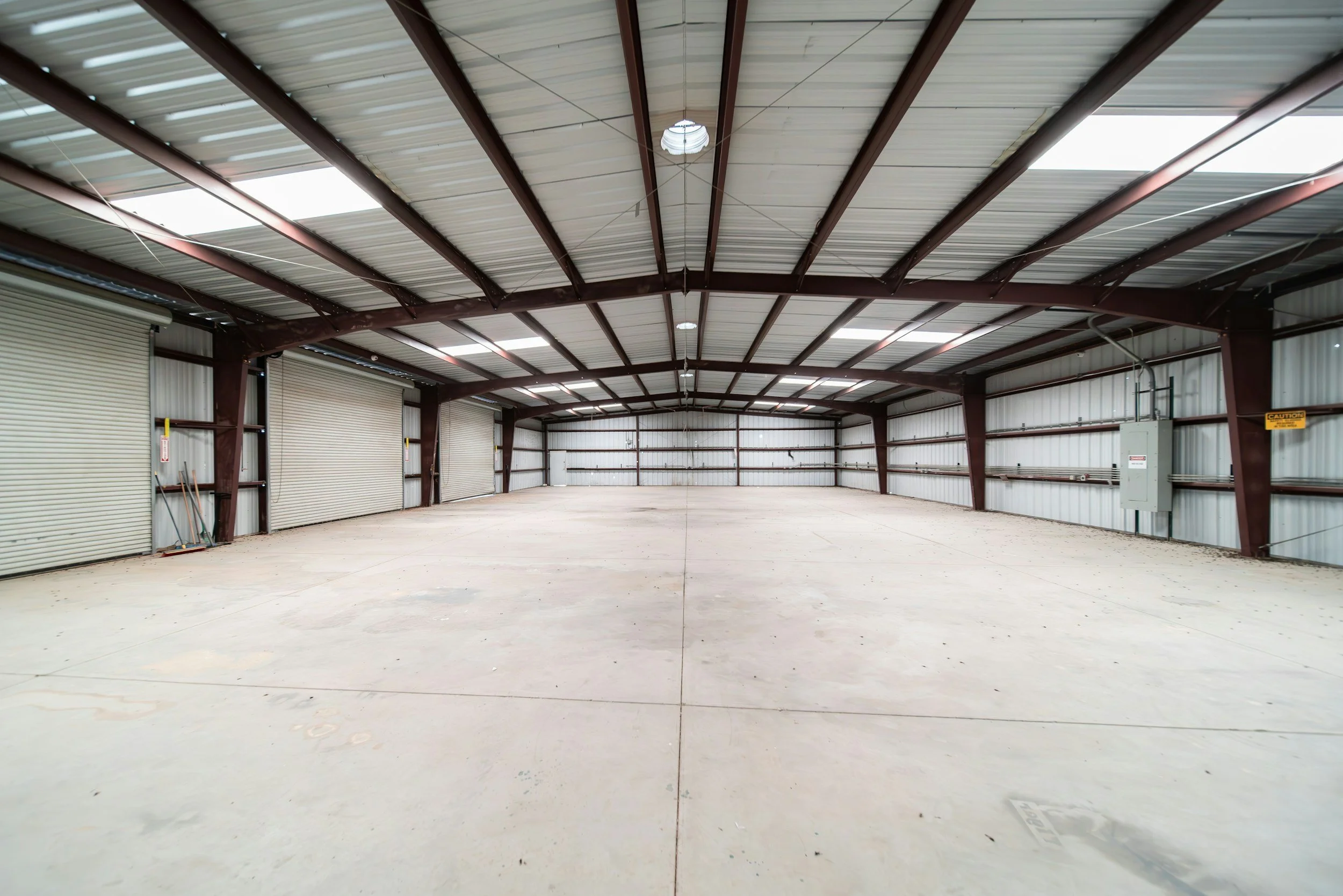 Empty commercial real estate warehouse with concrete floors and bright lights and open skylights.