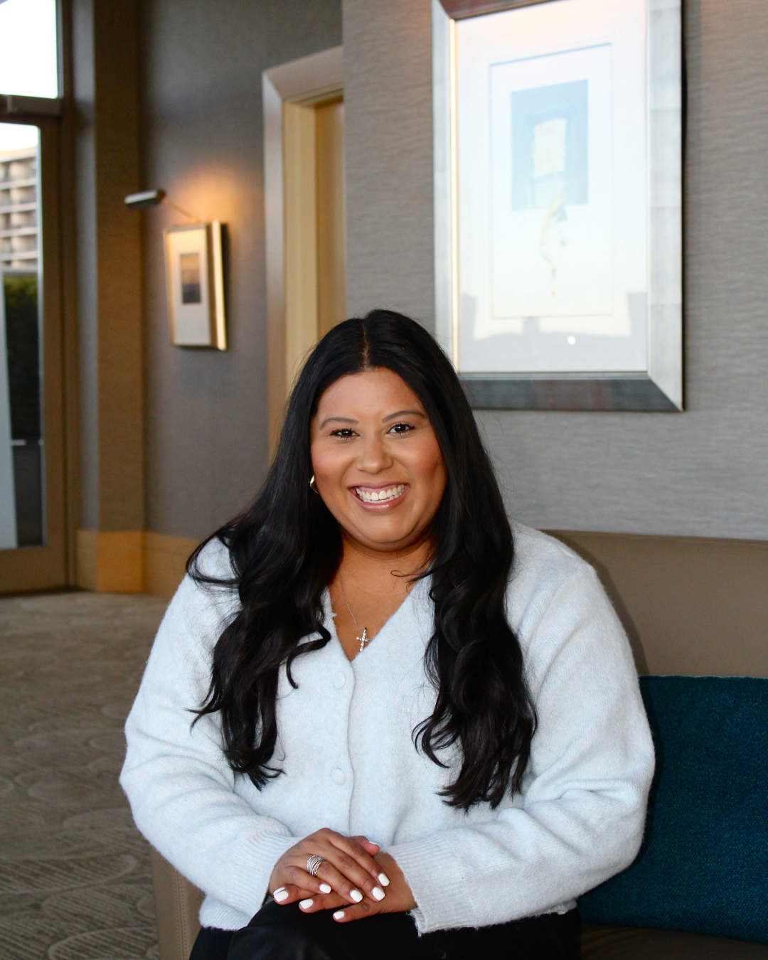 A woman with long black hair wearing a light blue sweater, sitting in a well-lit indoor setting, smiling at the camera.