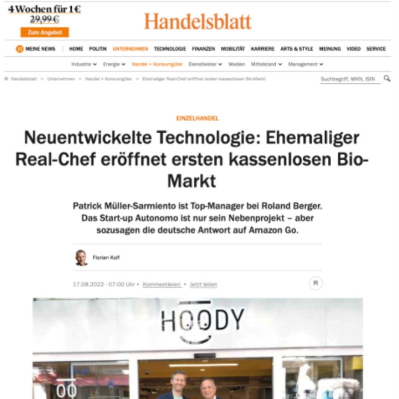 Screenshot einer Online-Zeitungsseite der Handelsblatt mit einem Artikel über eine neue Technologie im Bio-Markt, darunter ein Foto von zwei lachenden Männern vor einem Geschäft mit dem Namen 'HOODY'.