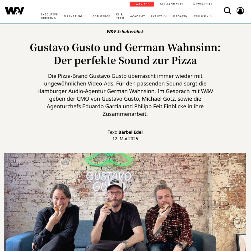 Drei Männer essen Pizza in einem trendigen Café mit Backsteinwand und Neon-Schriftzug 'GUSTAVO GUSTO' im Hintergrund.