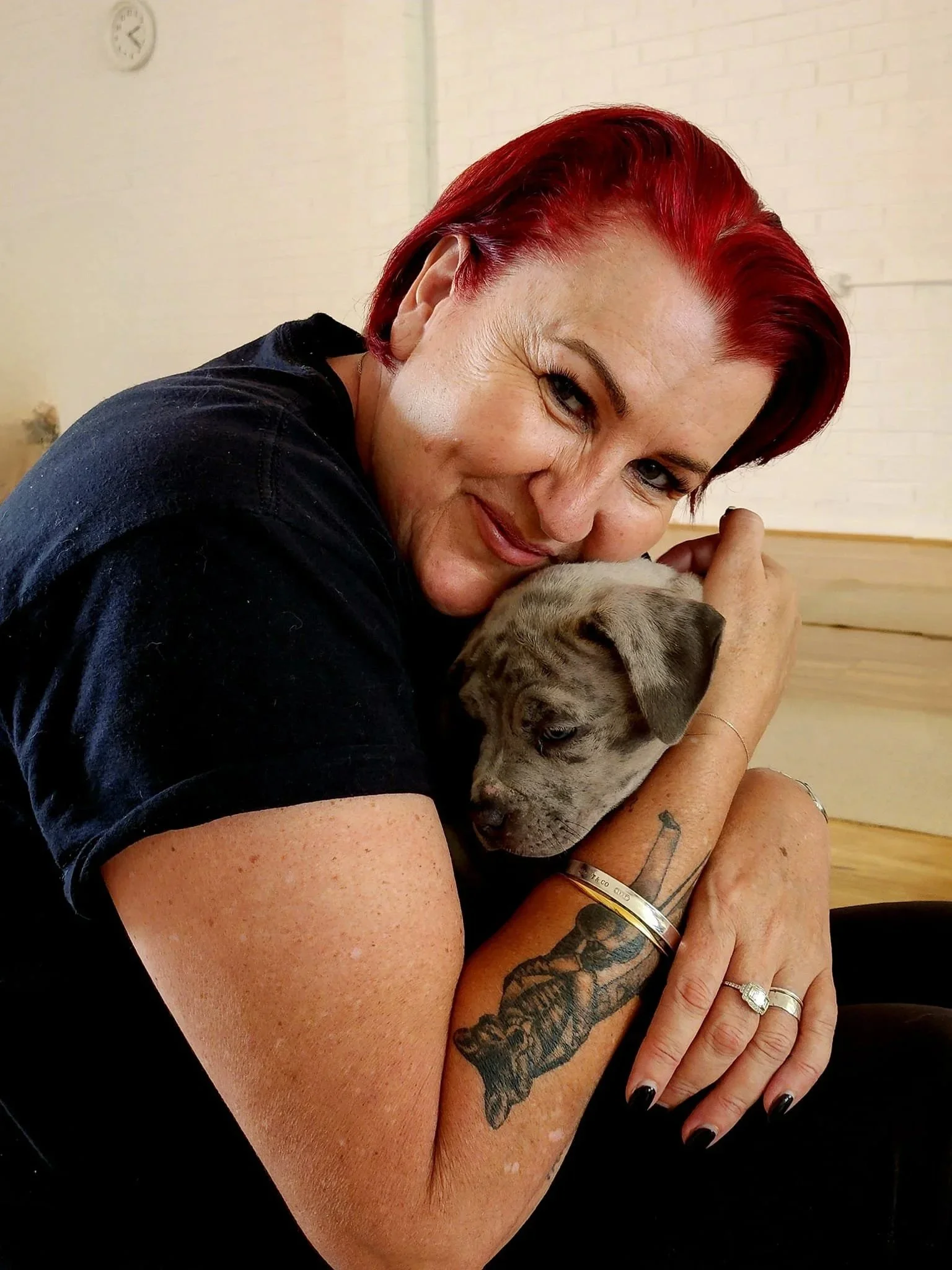 A woman with red hair holding a small, gray puppy close to her face, smiling and gently cradling the puppy's head.