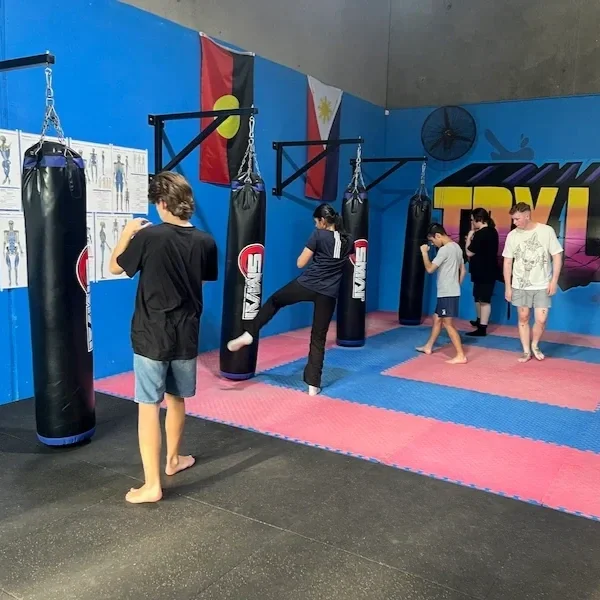 Four teens working on kicking the bags while a coach looks on.