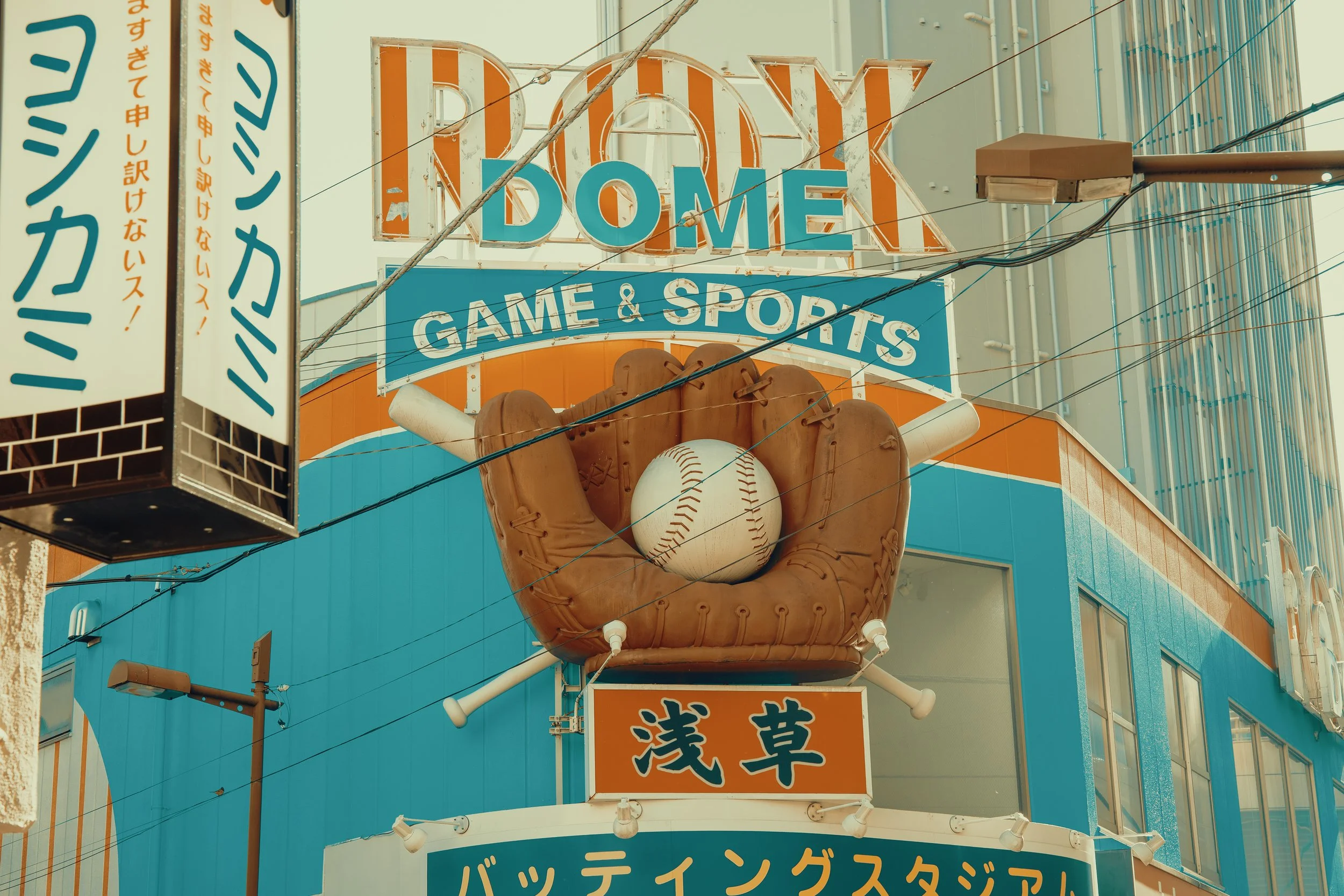 Signboard for Don Quijote store with a baseball-themed logo featuring a baseball glove holding a baseball on a city building facade.