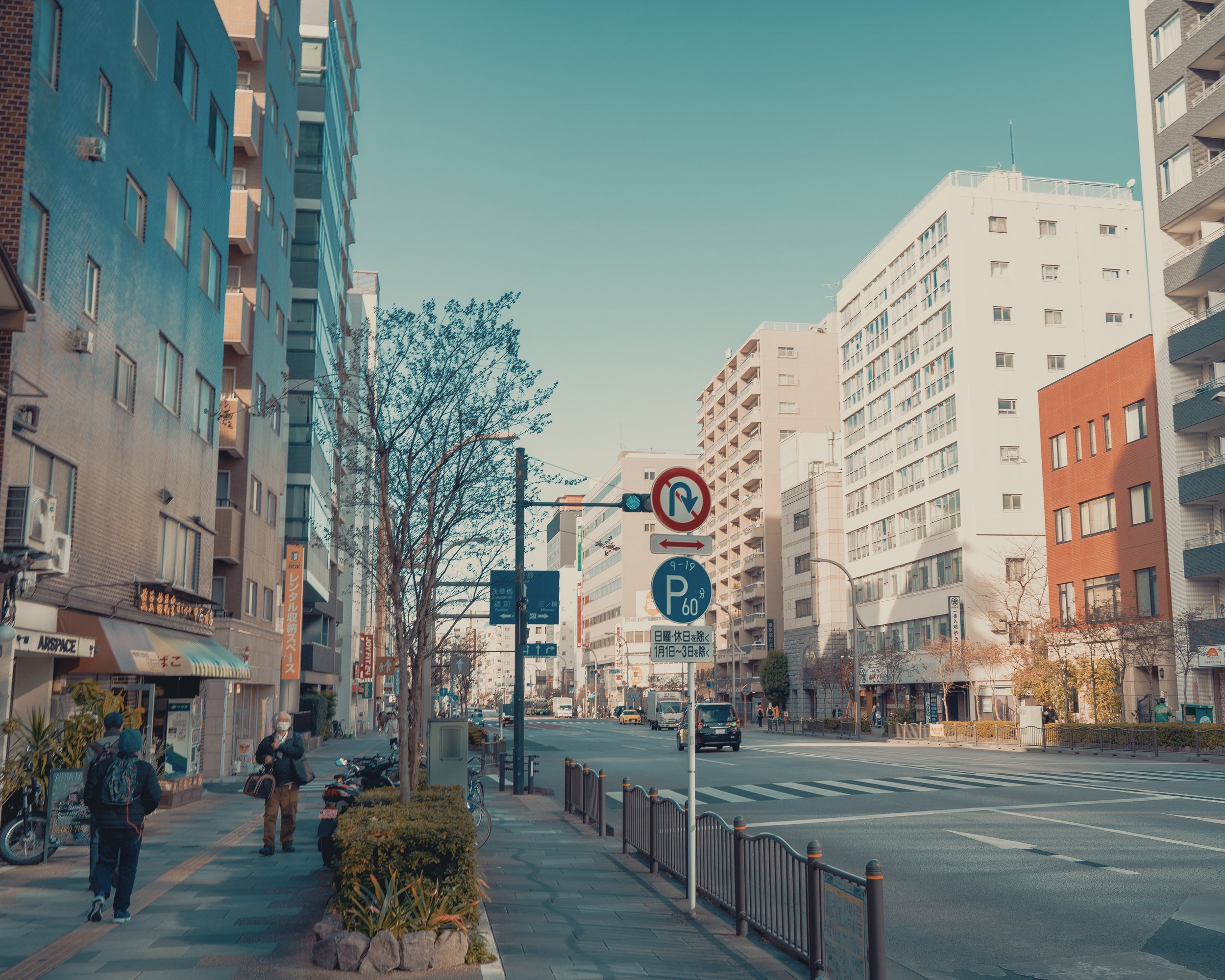 Urban street scene with tall buildings, pedestrians, and street signs indicating parking and no parking zones.