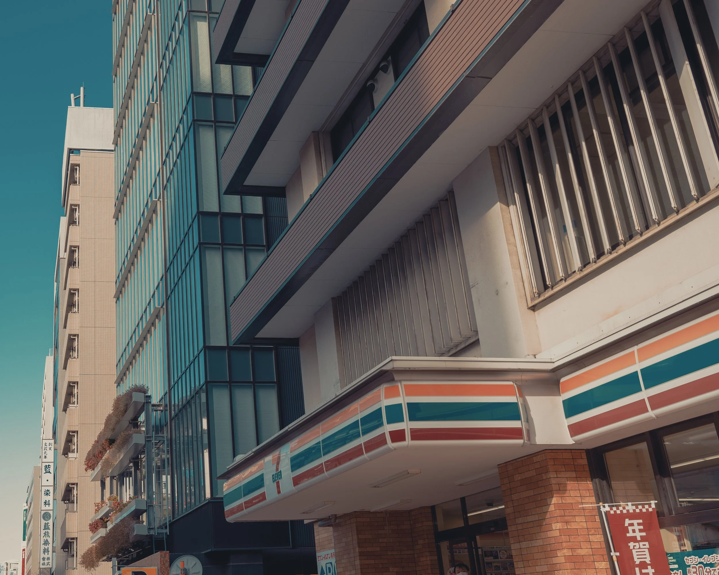 Urban street scene with a 7-Eleven convenience store on the ground floor of a multi-story building.