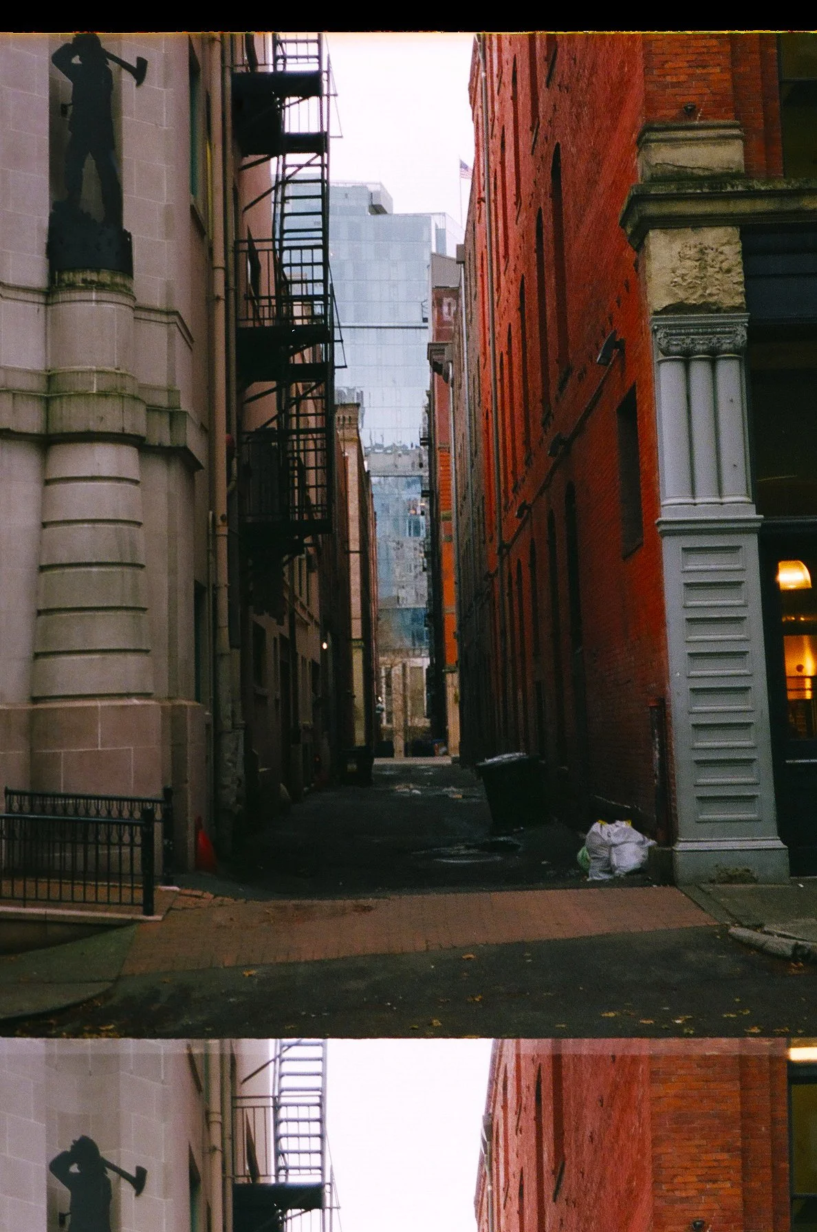 A narrow city alleyway between old brick and stone buildings with fire escapes, trash bags, and a garbage bin visible at the end.