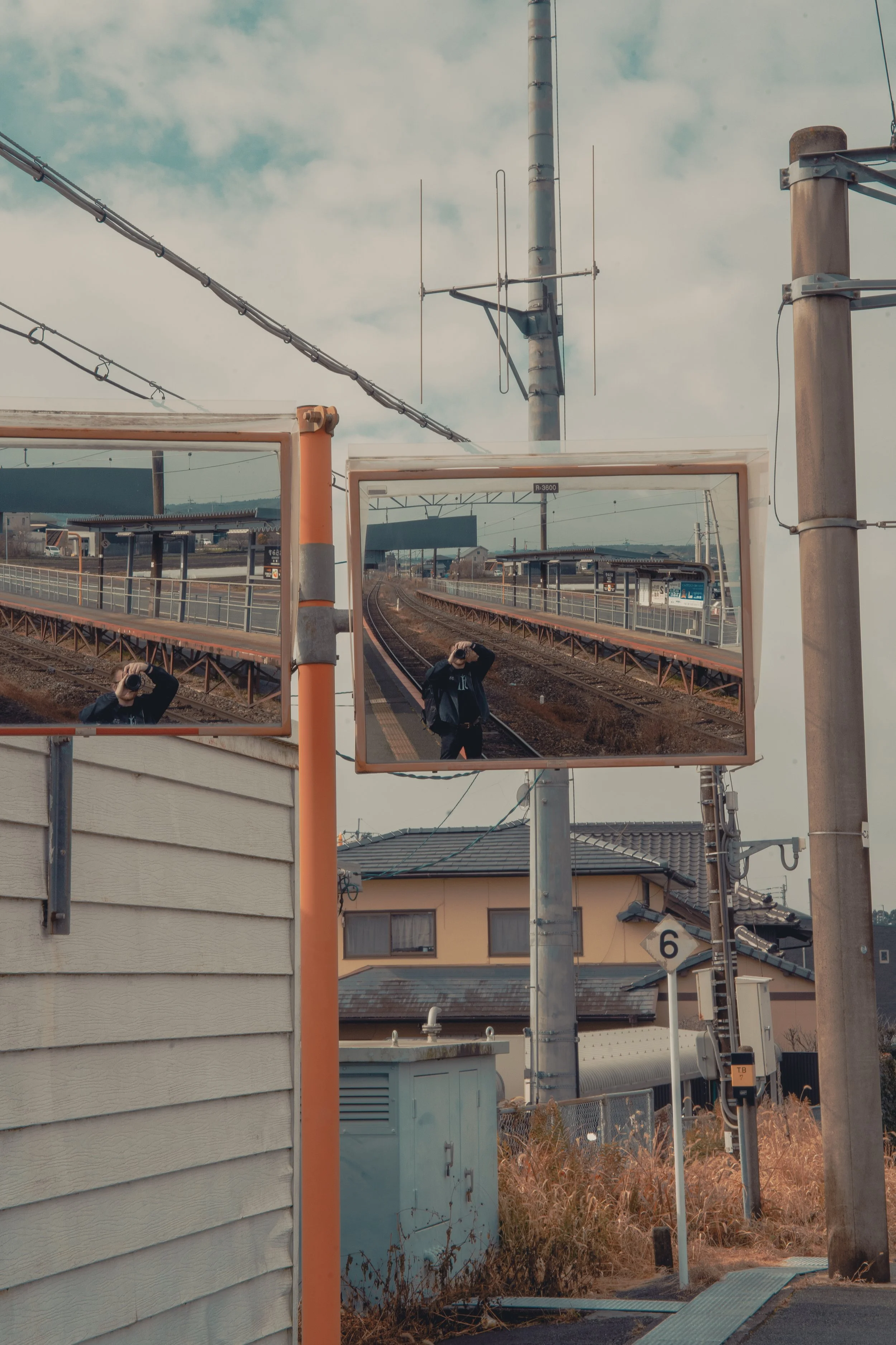 A train station with mirrors reflecting a person taking a photograph, with power lines and buildings in the background.