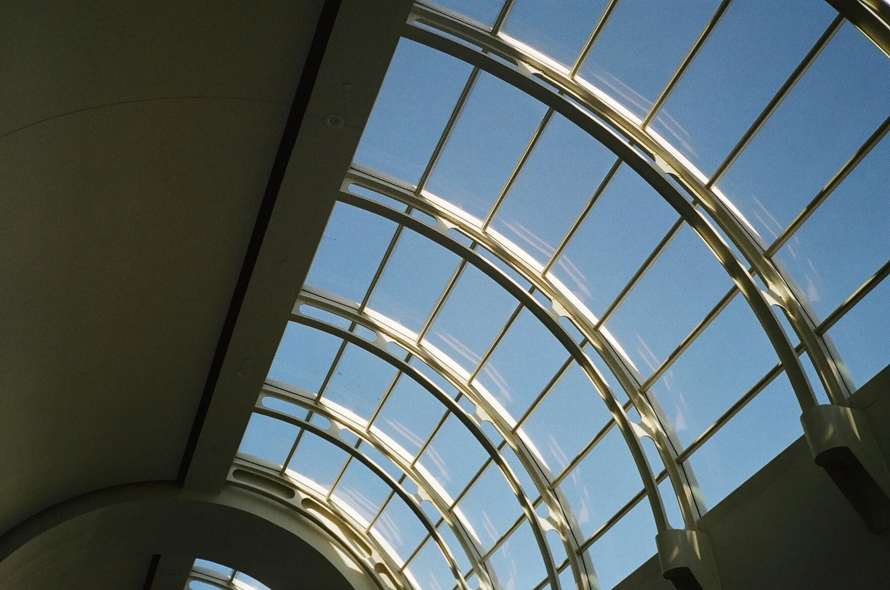 Interior view of a building with large arched glass skylights showing a blue sky with wispy clouds.
