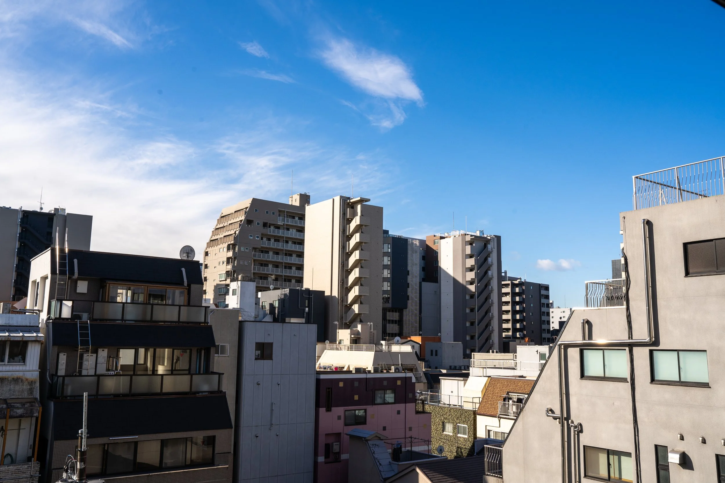 Cityscape of tall apartment buildings and office structures under a blue sky with wispy clouds.