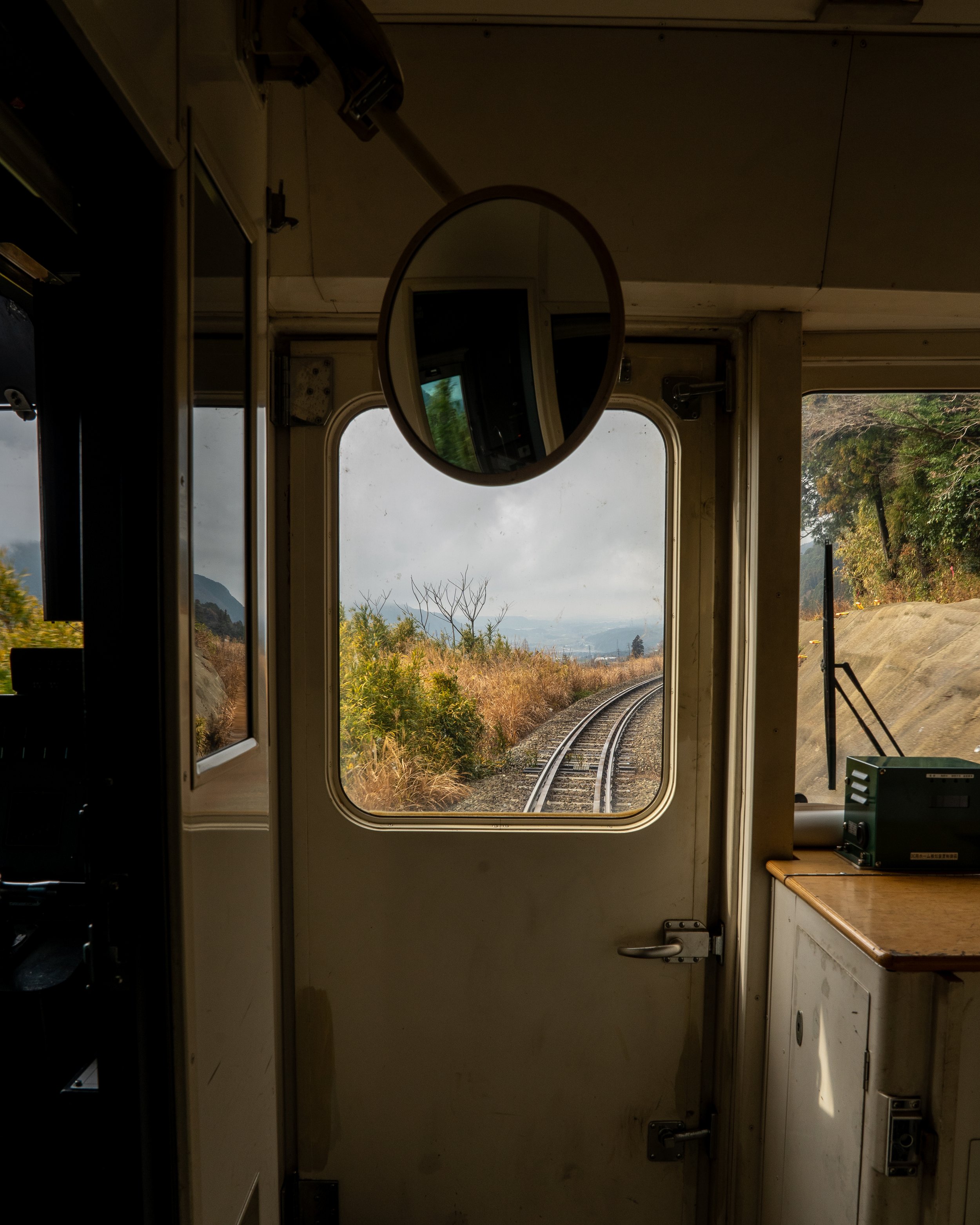 The view from inside a train cab looking out the front window at train tracks and countryside under cloudy sky.