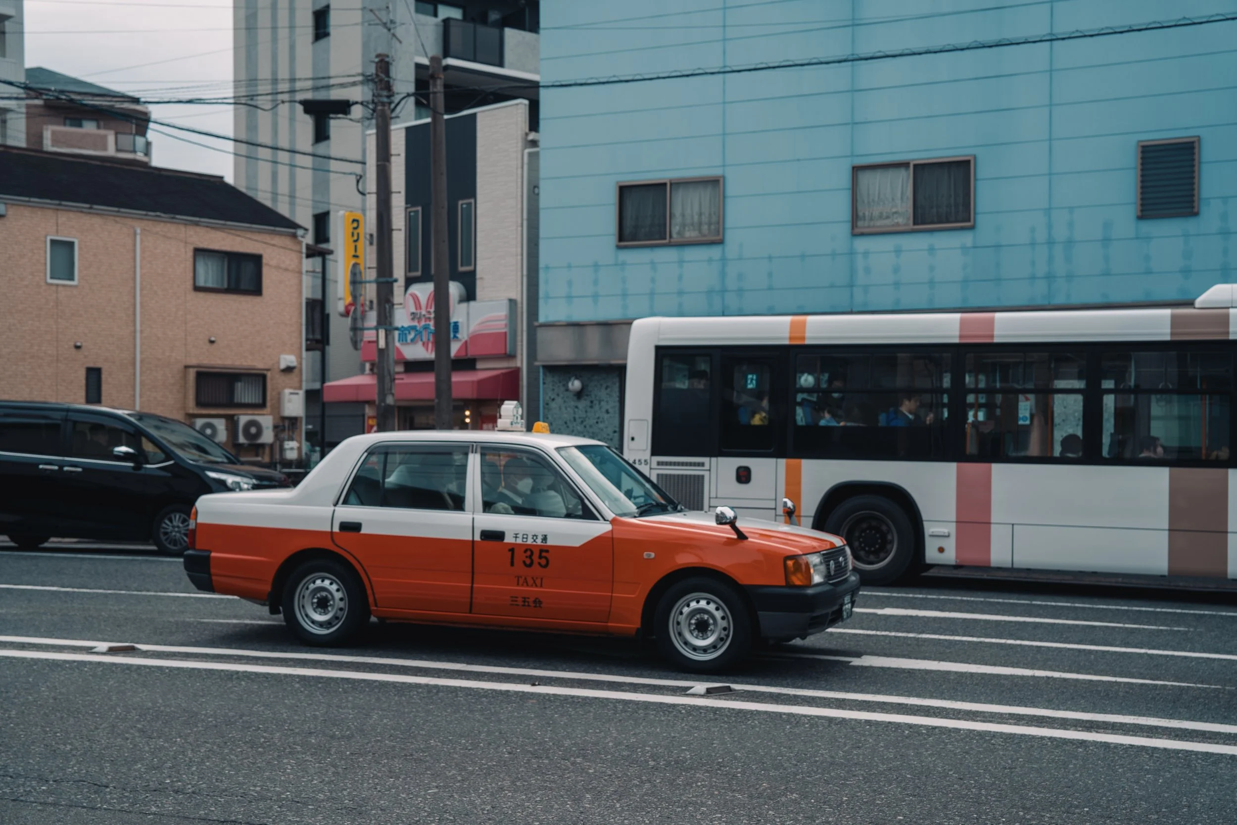 Street scene featuring a red and white taxi, a bus with passengers, and surrounding buildings in an urban area.