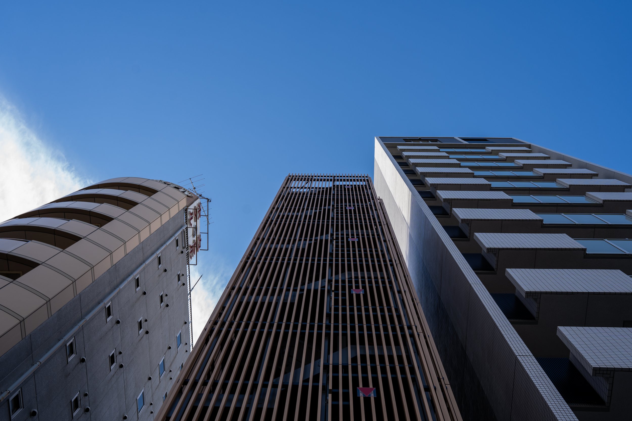 Looking up at three tall modern skyscrapers against a clear blue sky.
