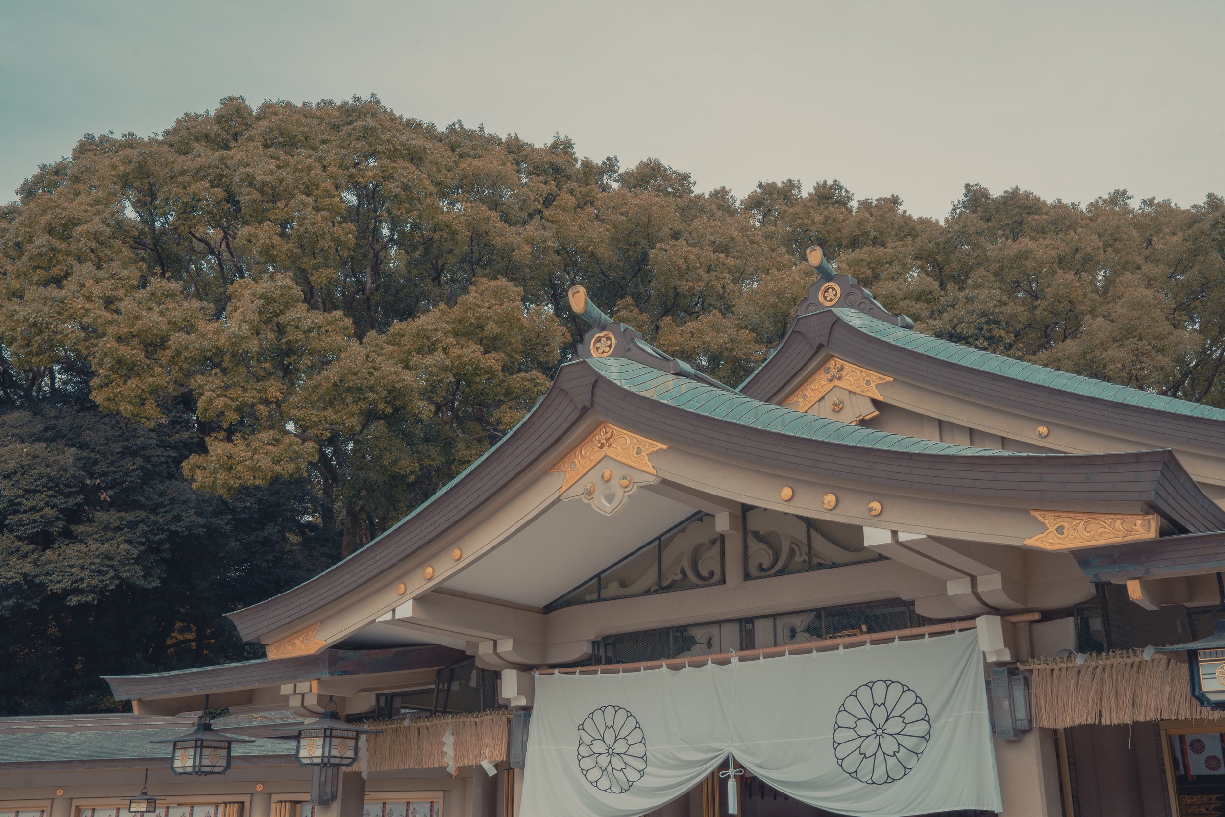 Traditional Japanese shrine with ornate roof, accompanied by decorative curtain and surrounded by trees.