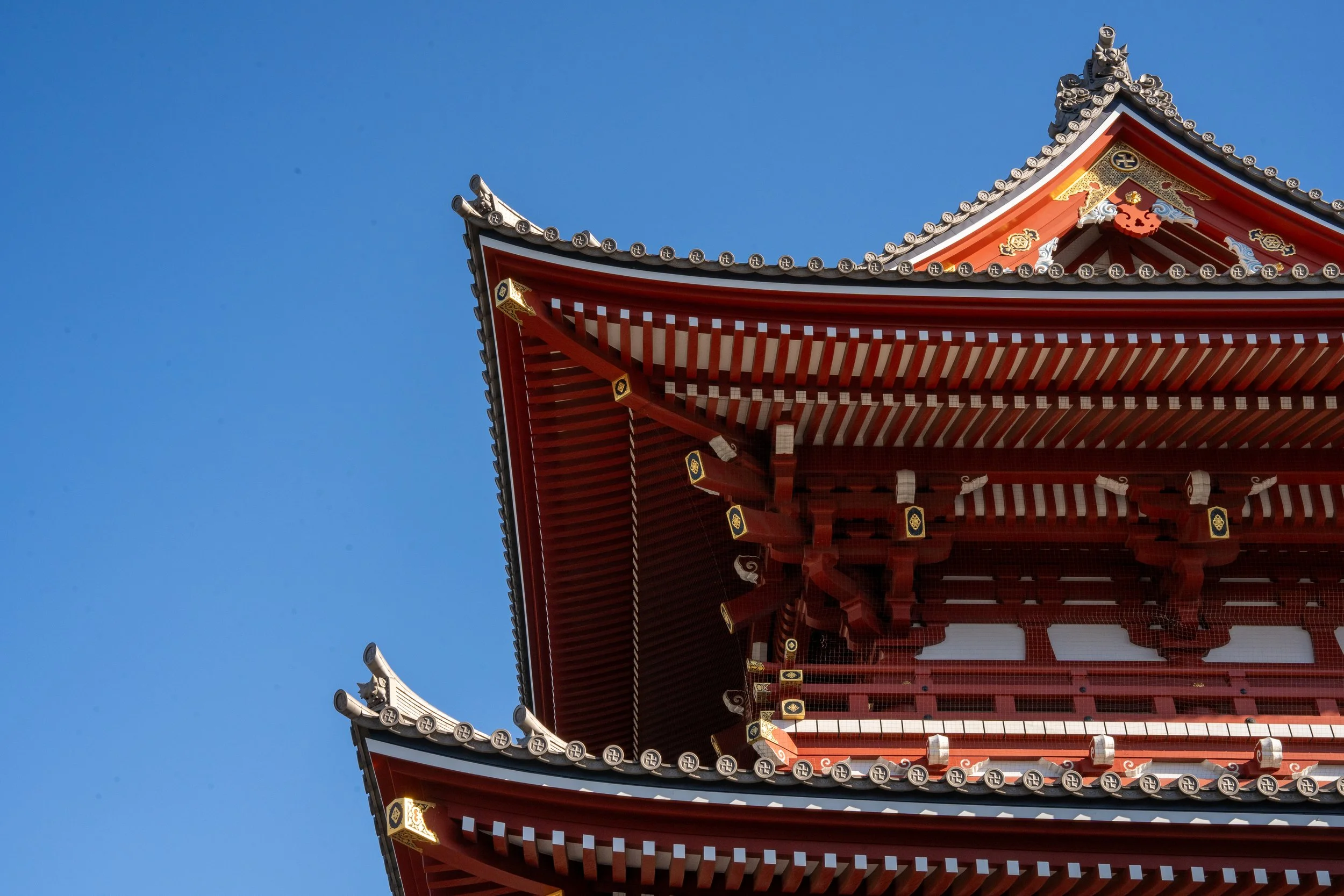 Close-up of the roof of a traditional Japanese pagoda with red wooden eaves and ornate details, against a clear blue sky.