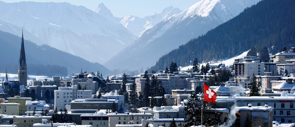 A snow-covered Swiss town with mountains in the background and a Swiss flag visible.