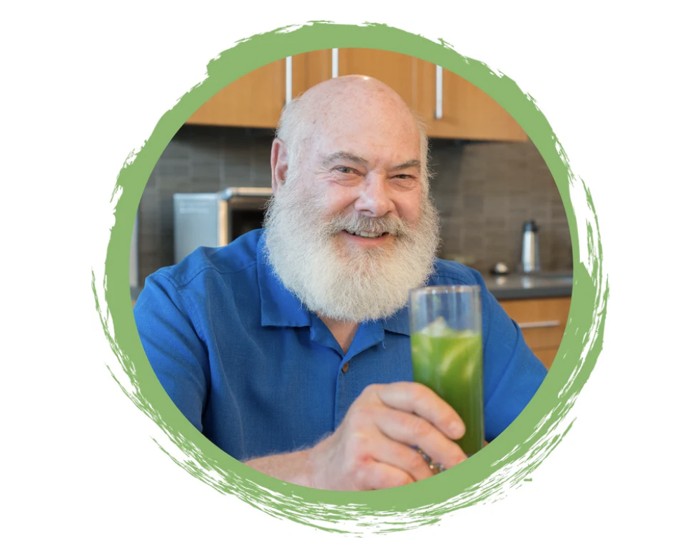 A bearded man in a blue shirt holding a green beverage, smiling in a kitchen setting with a circular green border around the image.