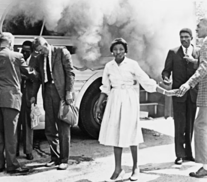 Black and white photo of people standing near a smoking bus, with one woman in a white dress holding hands with others.