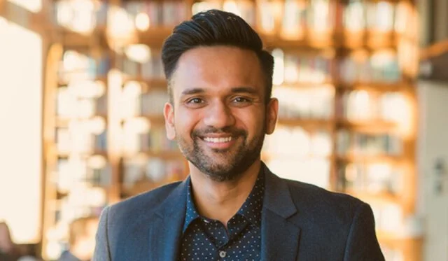 Smiling person in a blue blazer with a bookshelf in the background