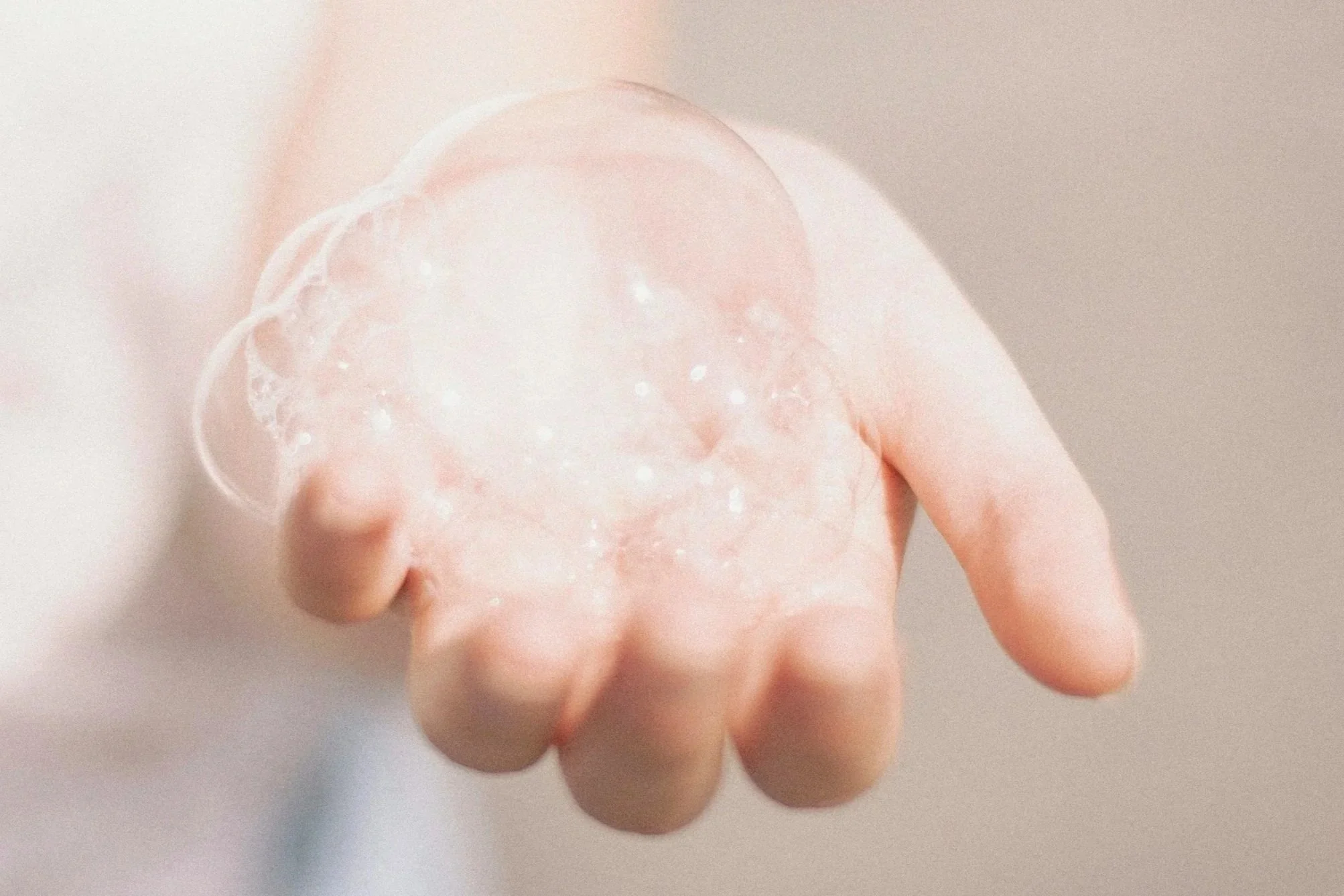 A hand holding a clear soap bubble with a blurred background