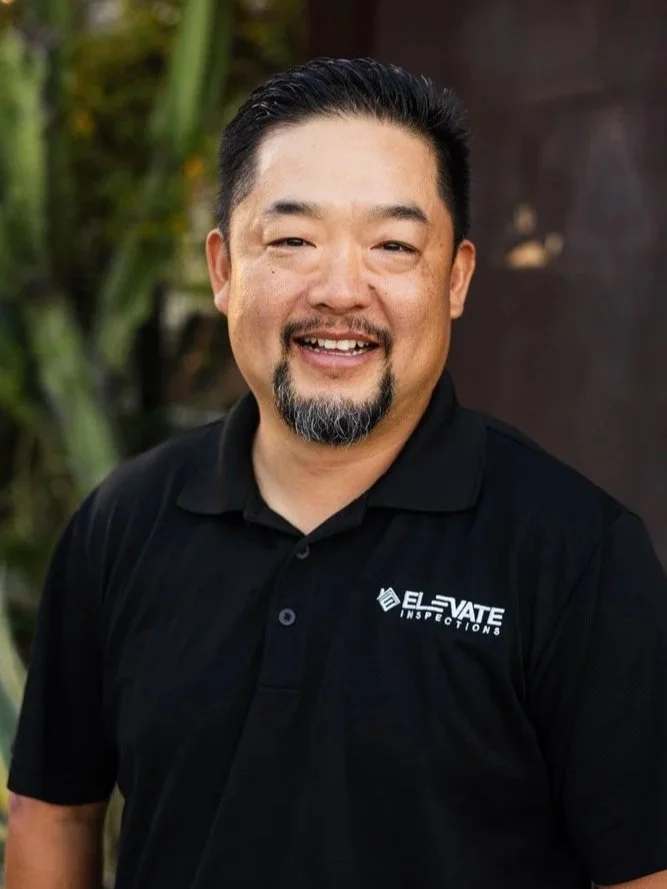 Portrait of a man with short dark hair and facial hair wearing a black collared shirt with 'BEN' embroidered on it and the logo 'ELEVATE INSPECTIONS'.