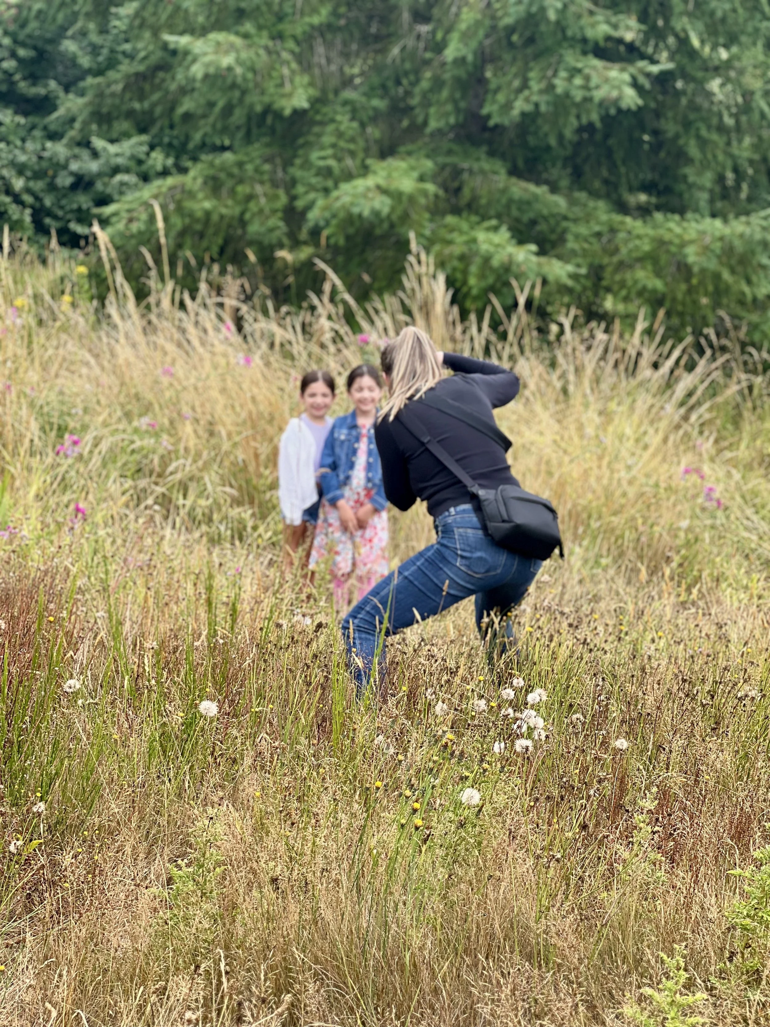 Emily taking a photo during a family photo shoot in a mid-summer field with sister.