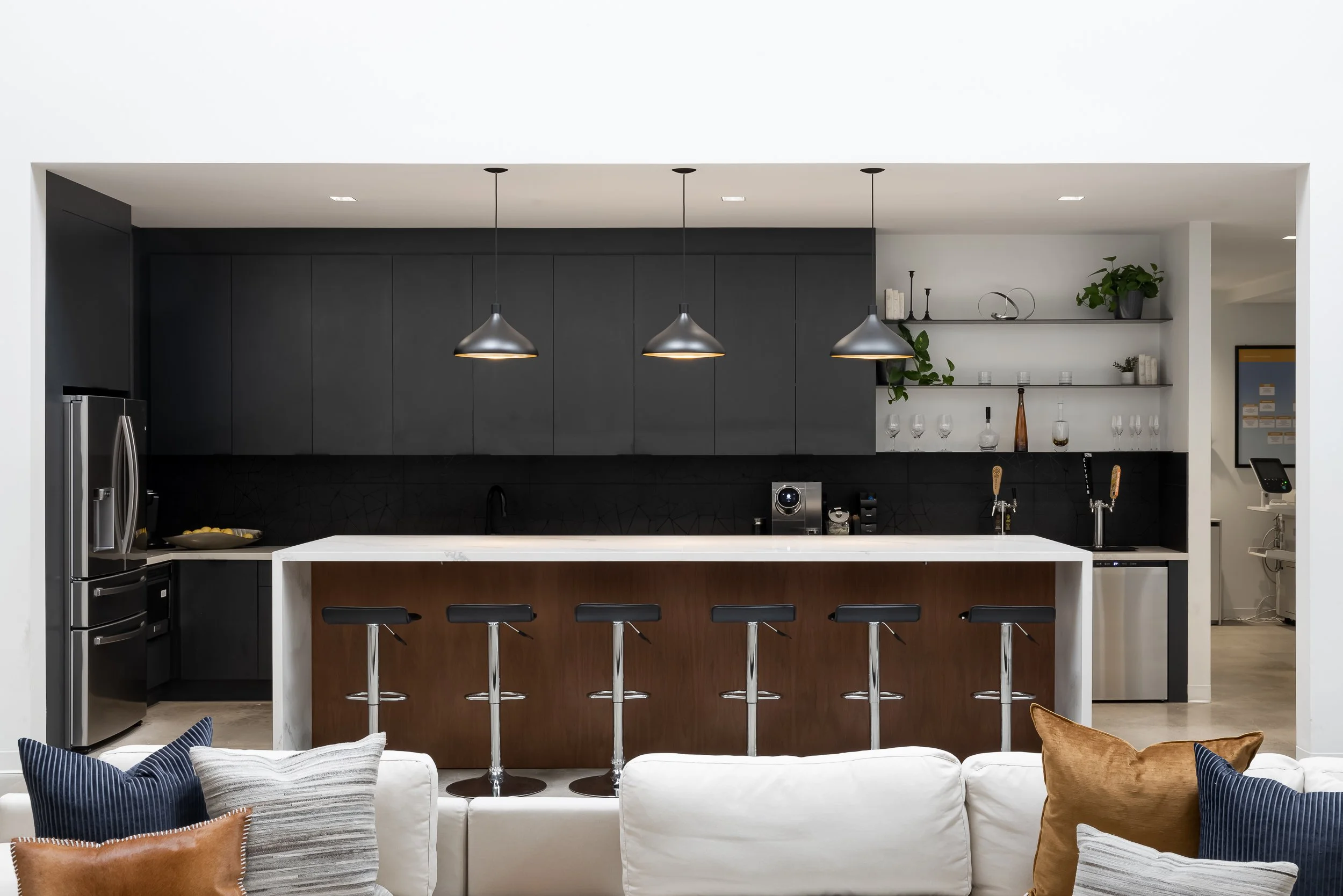 Modern kitchen with black cabinets, white island with wooden base, three pendant lights, and open shelving with decor and plants.
