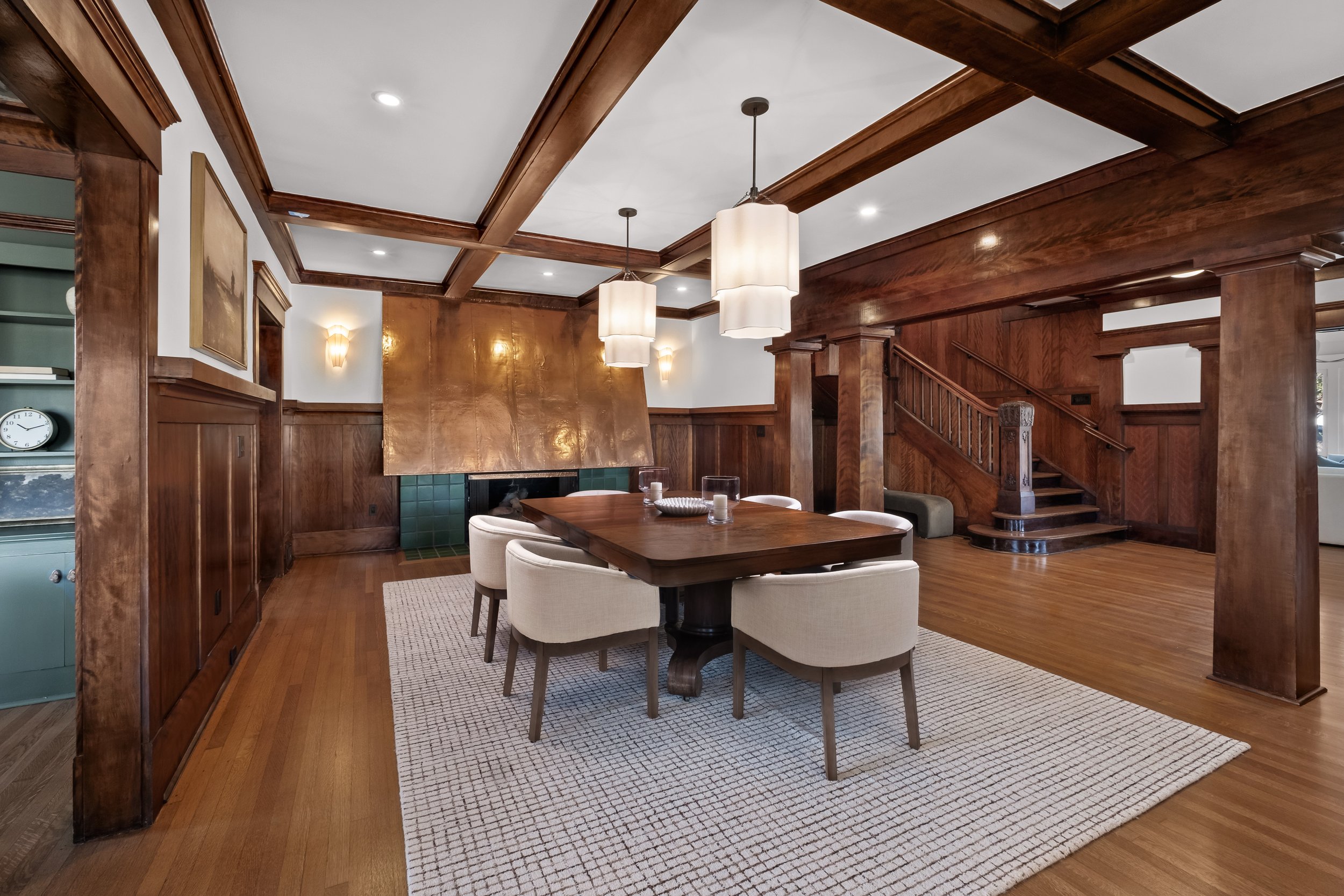 Dining room with a wooden table, upholstered chairs, wood-paneled walls, a white rug, and modern hanging pendant lights.