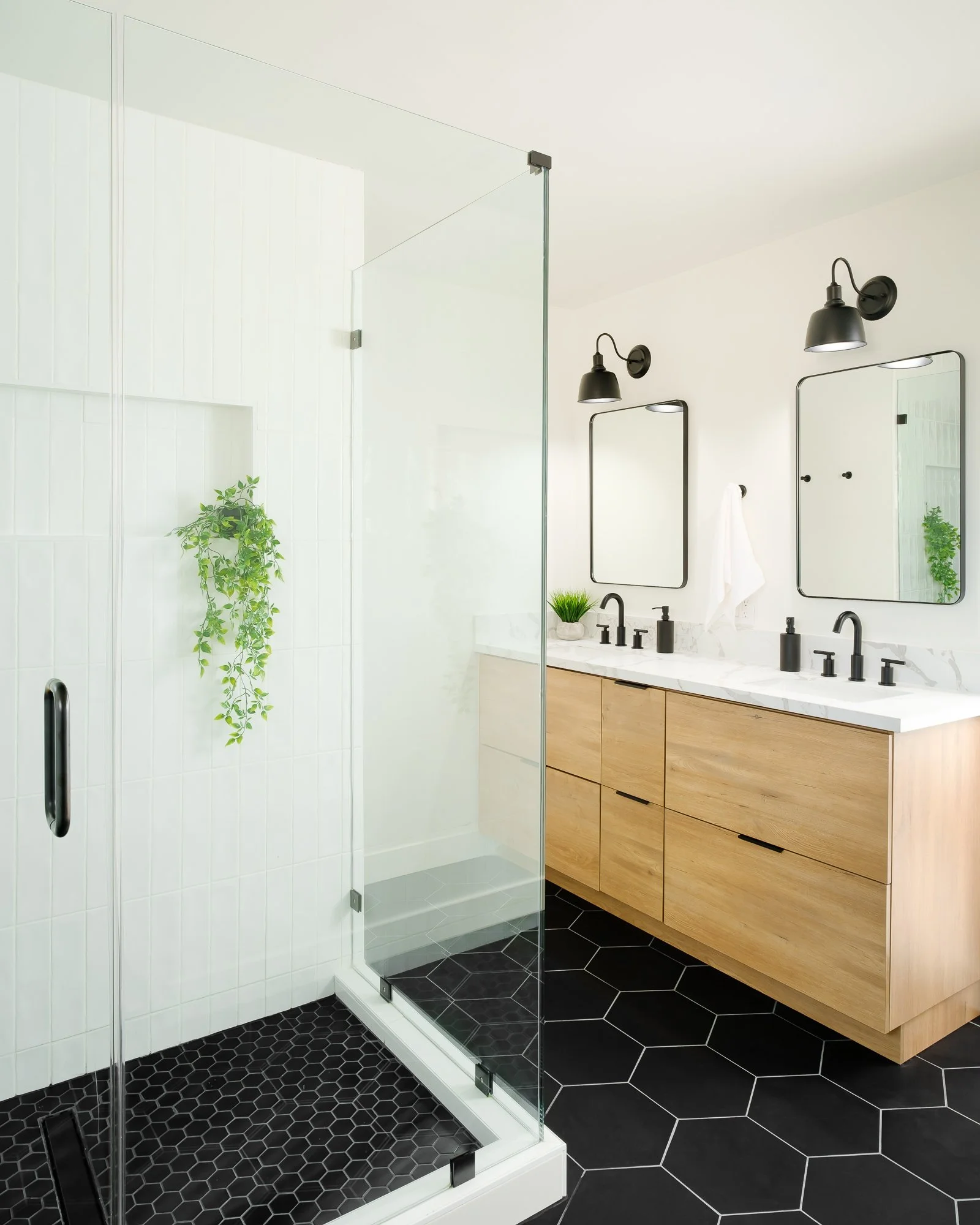 Modern bathroom with black hexagonal floor tiles, a glass shower enclosure, a wooden vanity with black fixtures, and large mirrors.