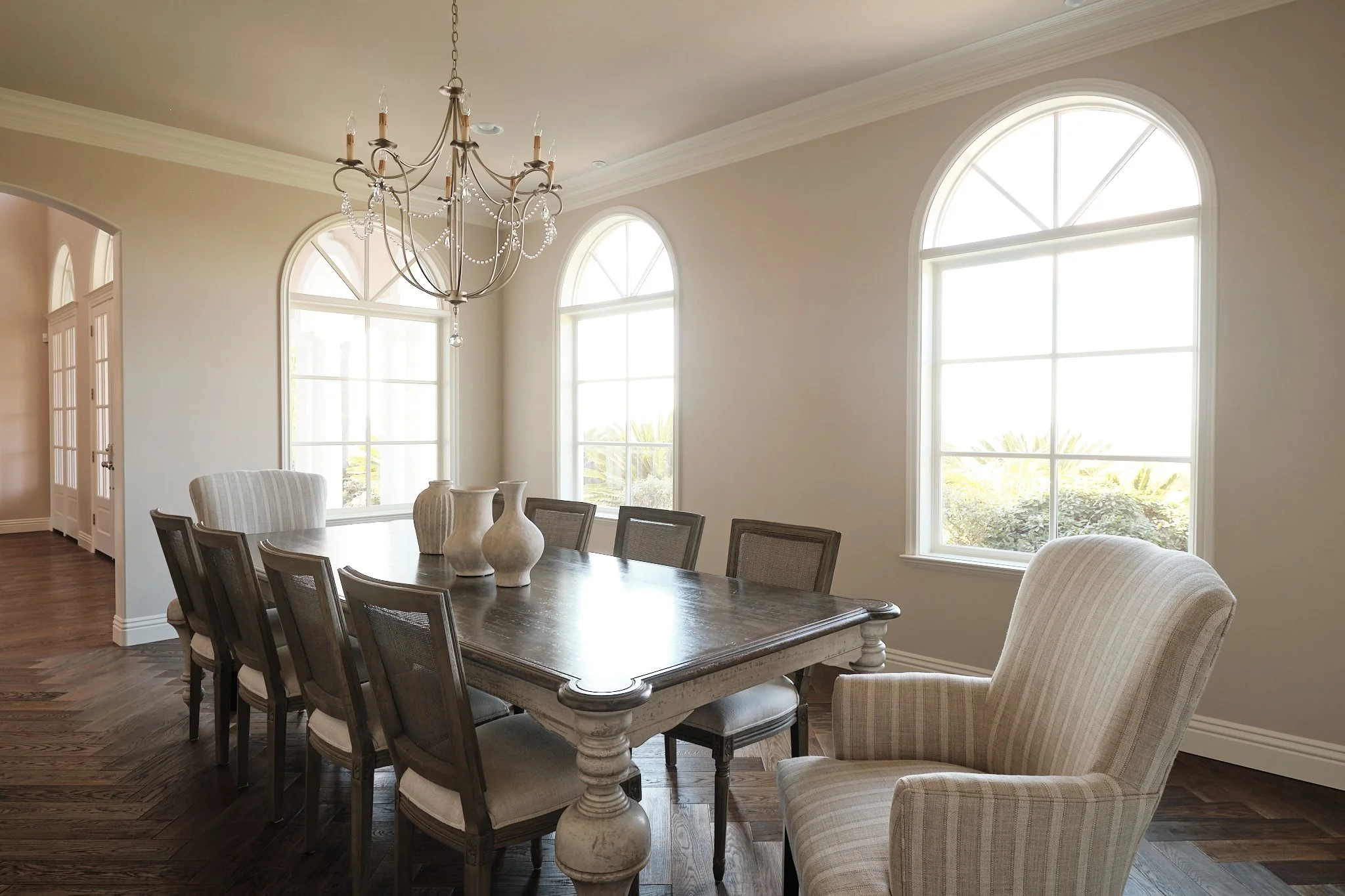 Dining room with large arched windows, chandelier, wooden dining table, and chairs.