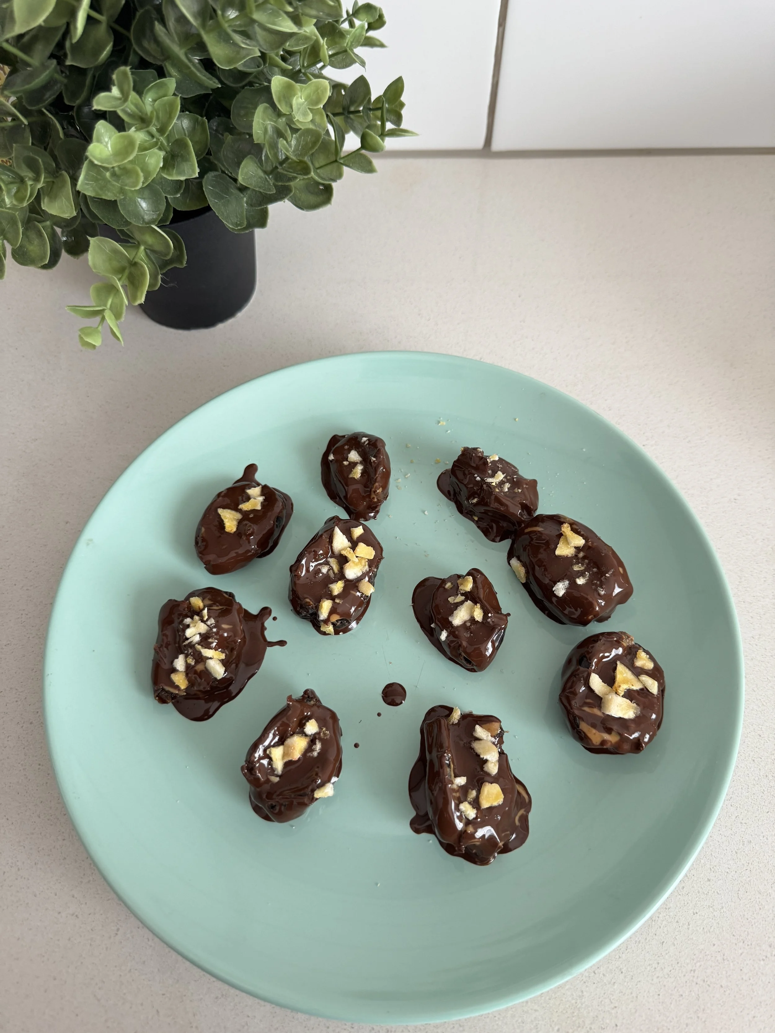 Snicker dates on a teal plate sitting on the kitchen counter next to a green plant.