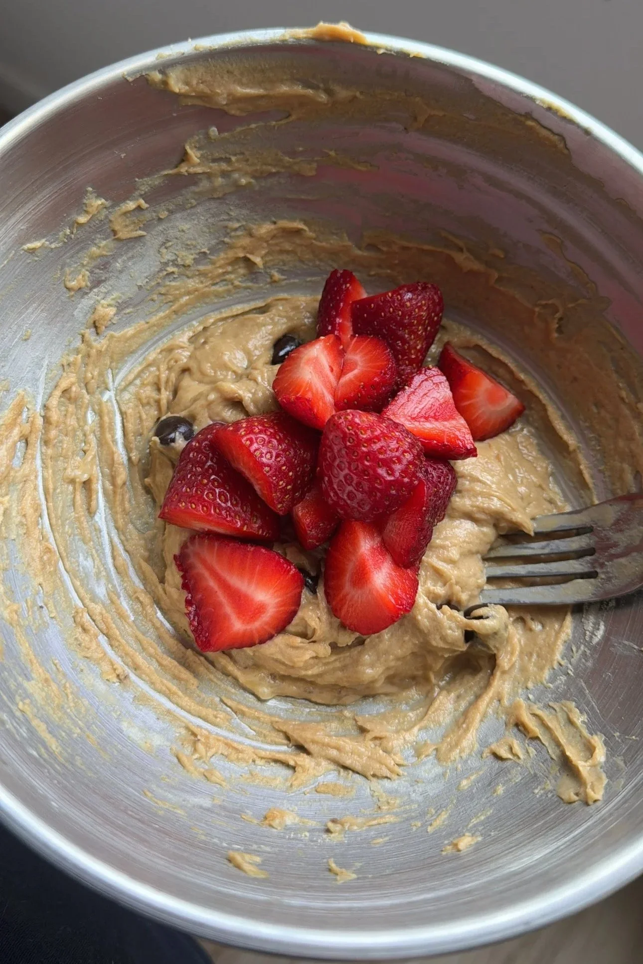 Protein cookie dough with some strawberries in a metal medium mixing bowl.
