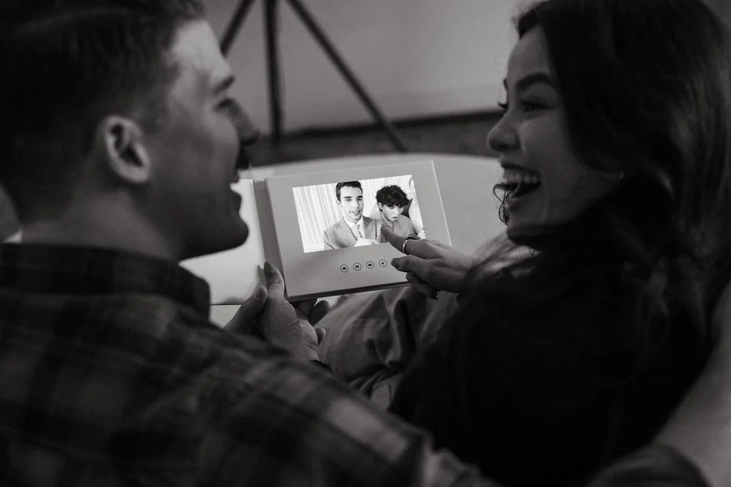 A smiling couple looking at a small photo album together, sitting close to each other indoors.