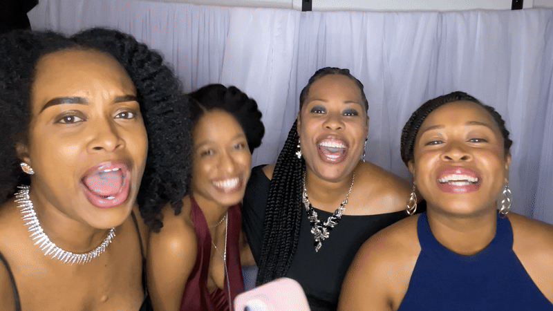 Four women smiling and posing for a photo, dressed in formal attire.