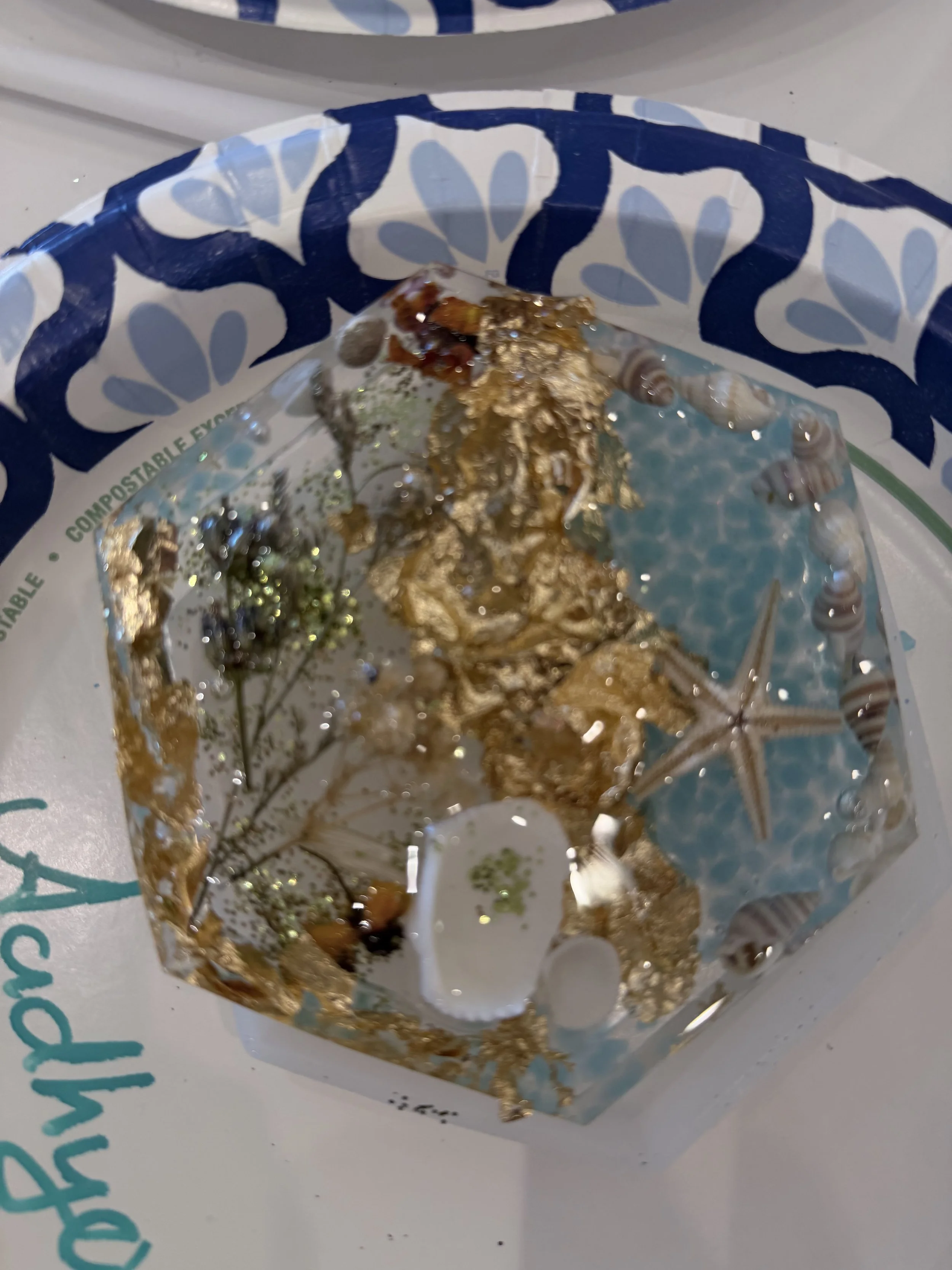 A gold foil wrapped chocolate or candy sitting on a white surface with blue and green text, partially visible, near the bottom of the image.