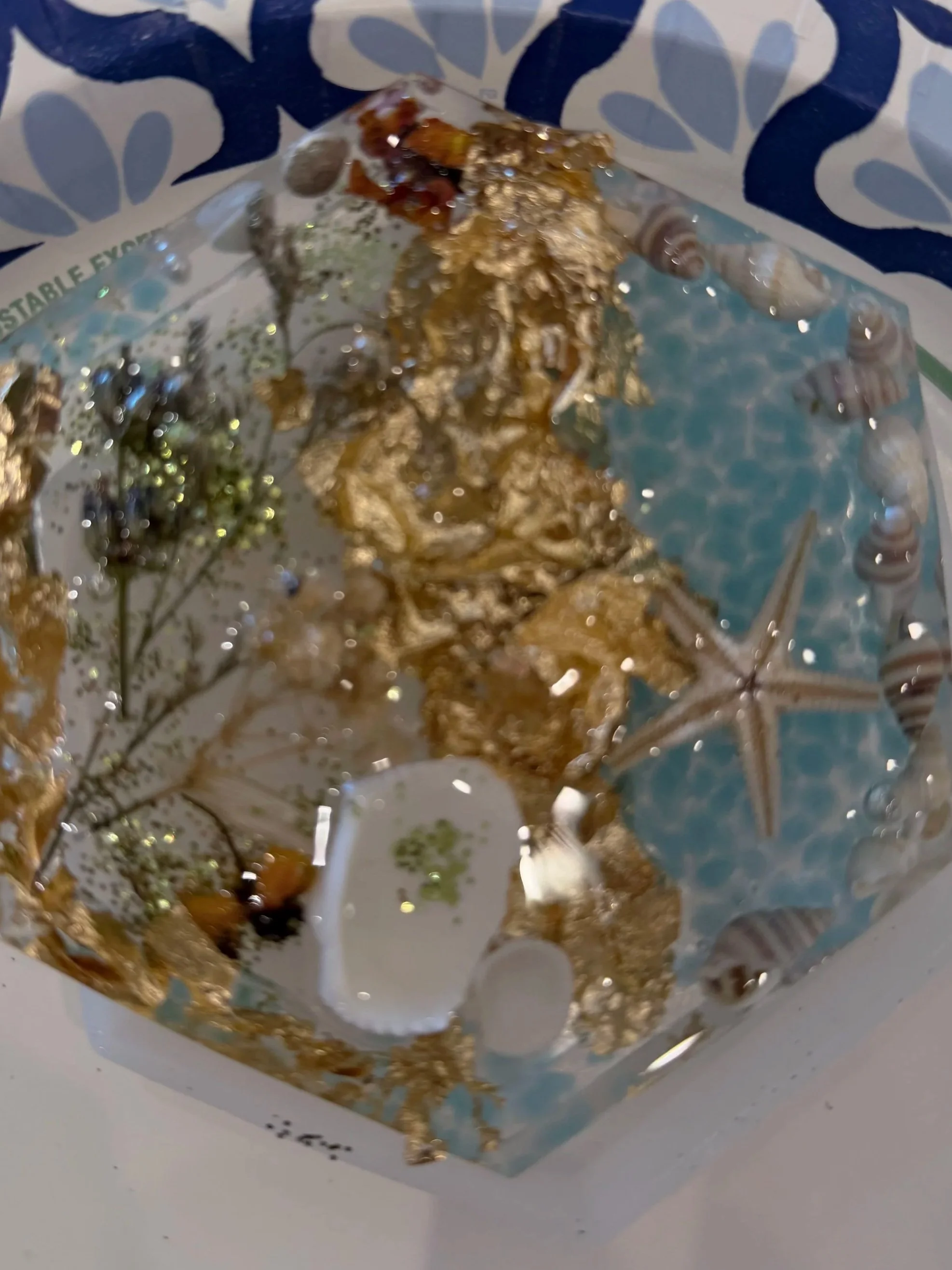 Close-up of a decorative paper featuring gold foil accents, seashells, starfish, and floral patterns.