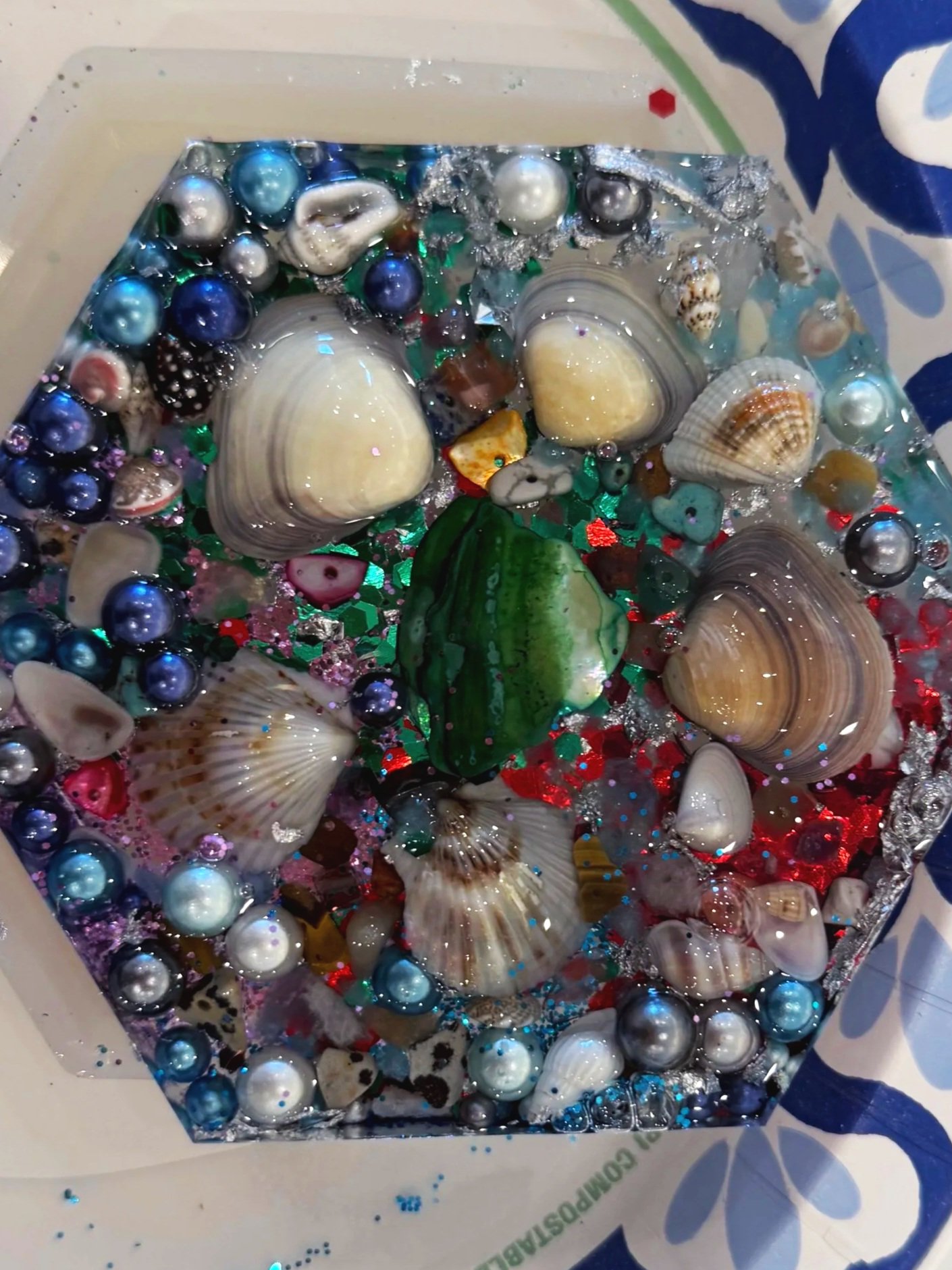 Close-up of a piñata filled with decorative shells and beads on a plastic plate, with a decorative paper border with blue and white patterns.