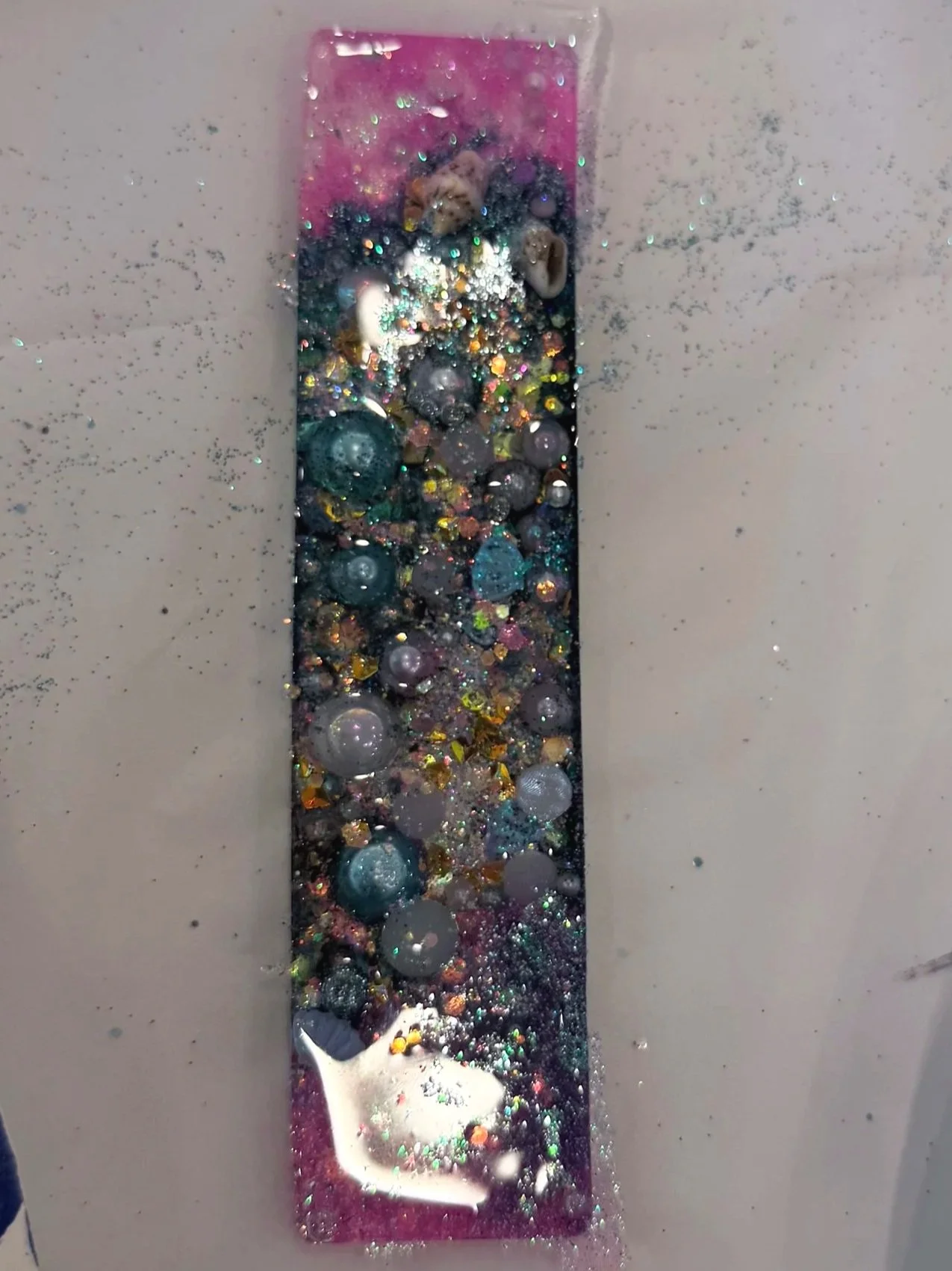 A tray with spilled glitter, beads, and small craft items, some on a paper plate with a blue and white pattern, on a white surface.