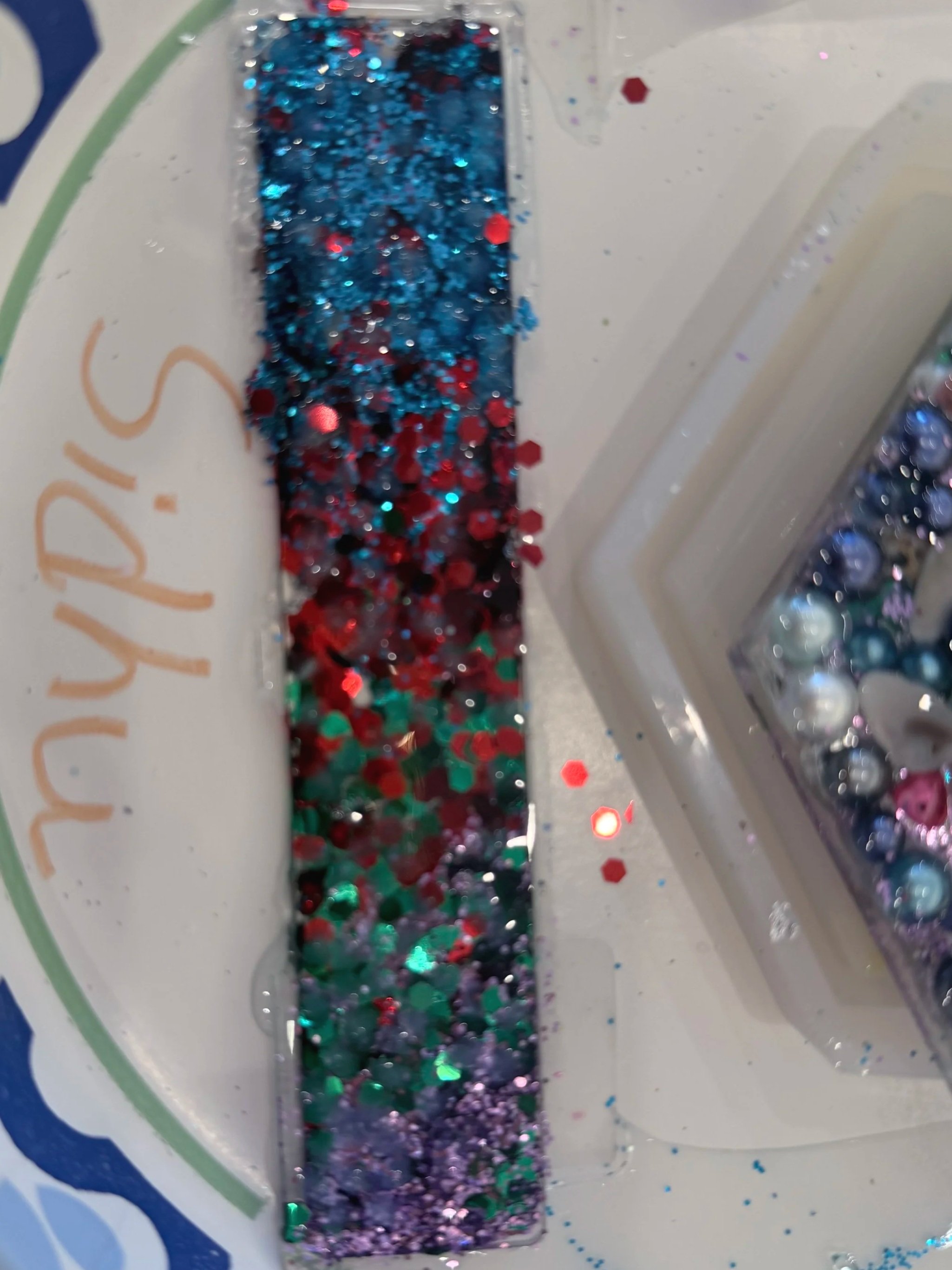 Close-up of red, blue, purple, and silver glitter in a clear plastic container on a white plate with blue decorative pattern.