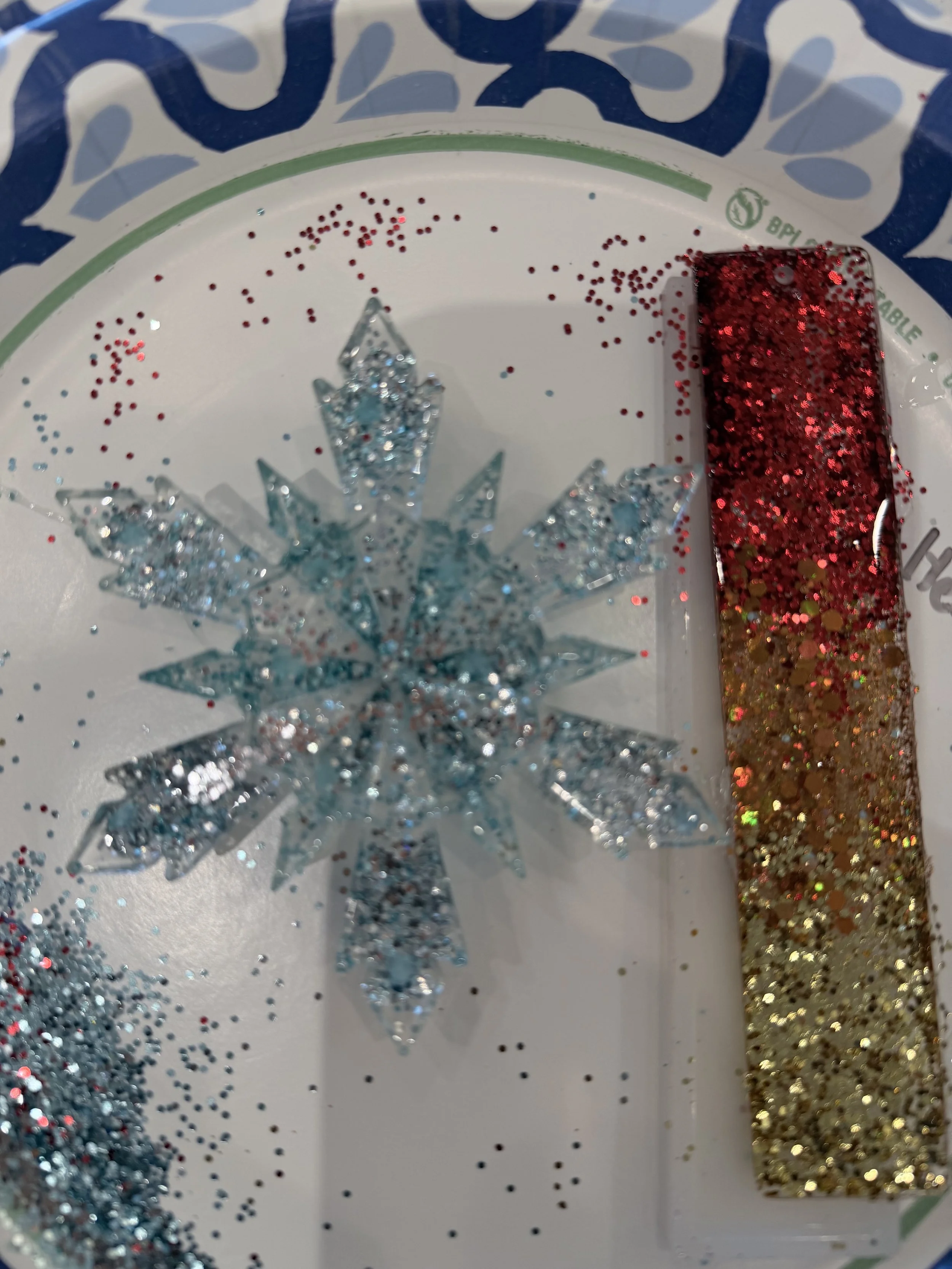 Decorative large snowflake ornament with glitter, red and gold glitter, and scattered red, blue, and gold confetti on a white tray with a blue and white patterned border.