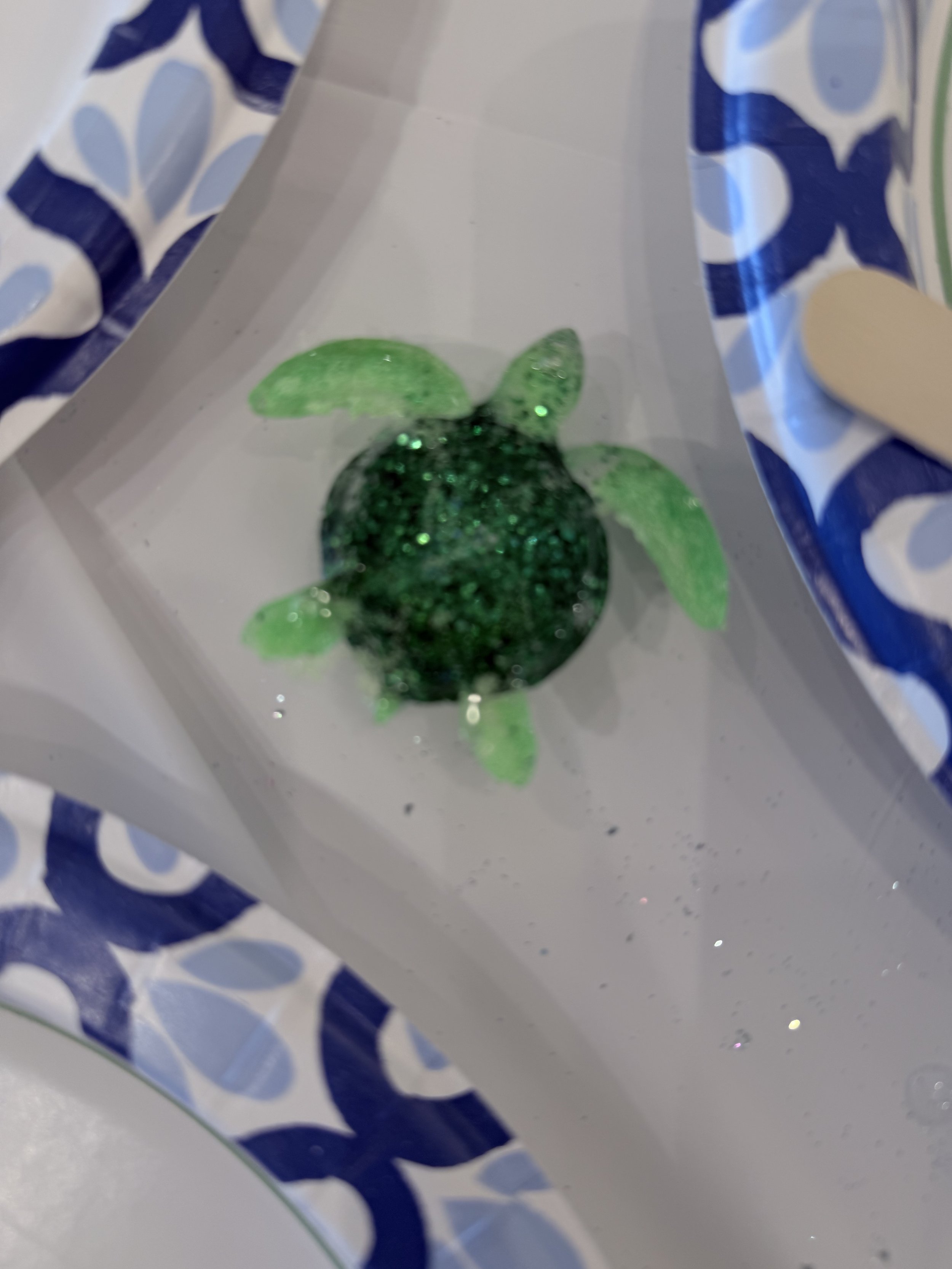 Close-up view of a sparkly green fish-shaped decorative item inside a paper bag with blue and white patterns.