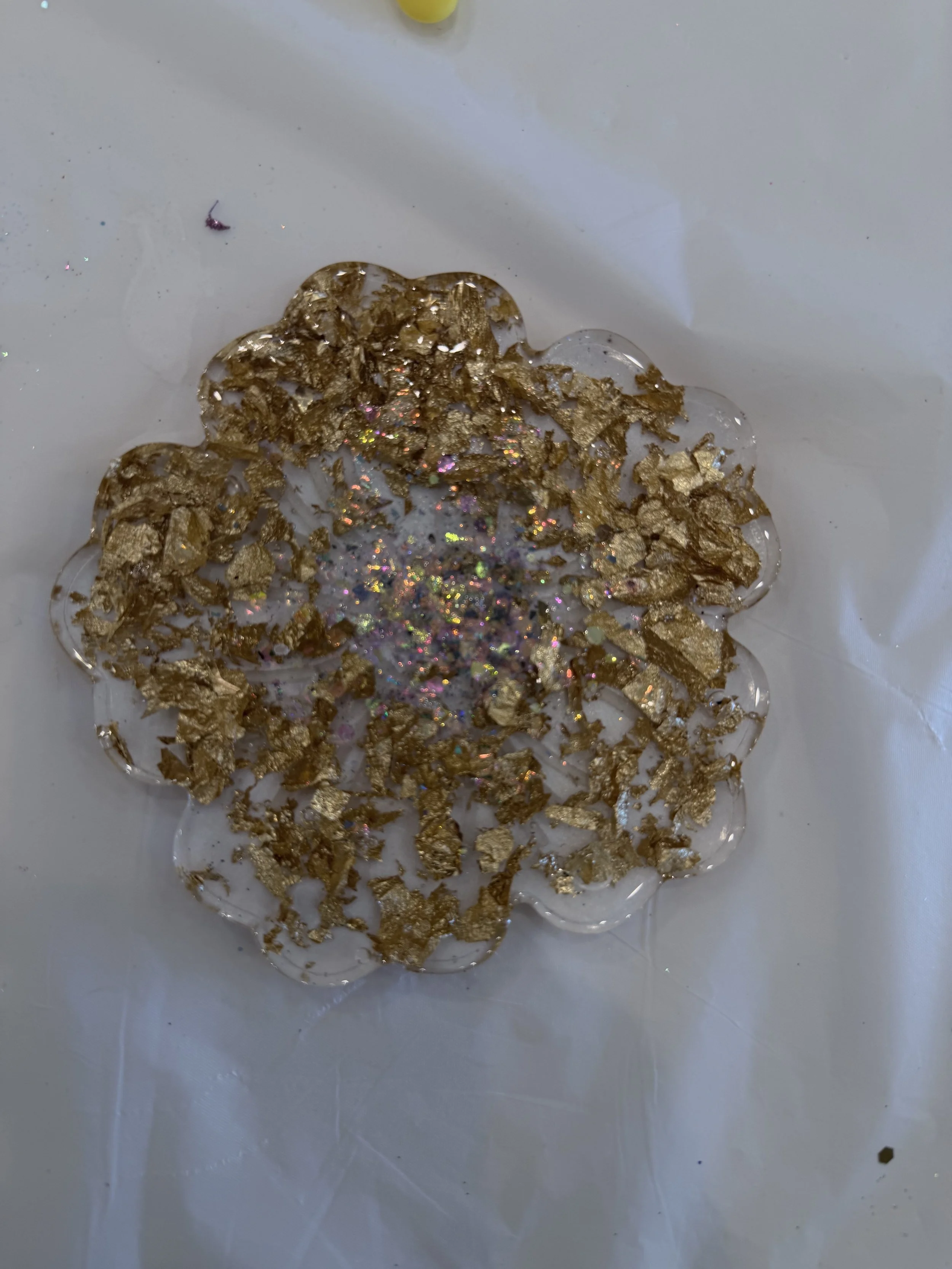 Close-up of a decorated snowflake craft made with gold foil and holographic glitter on a white surface.