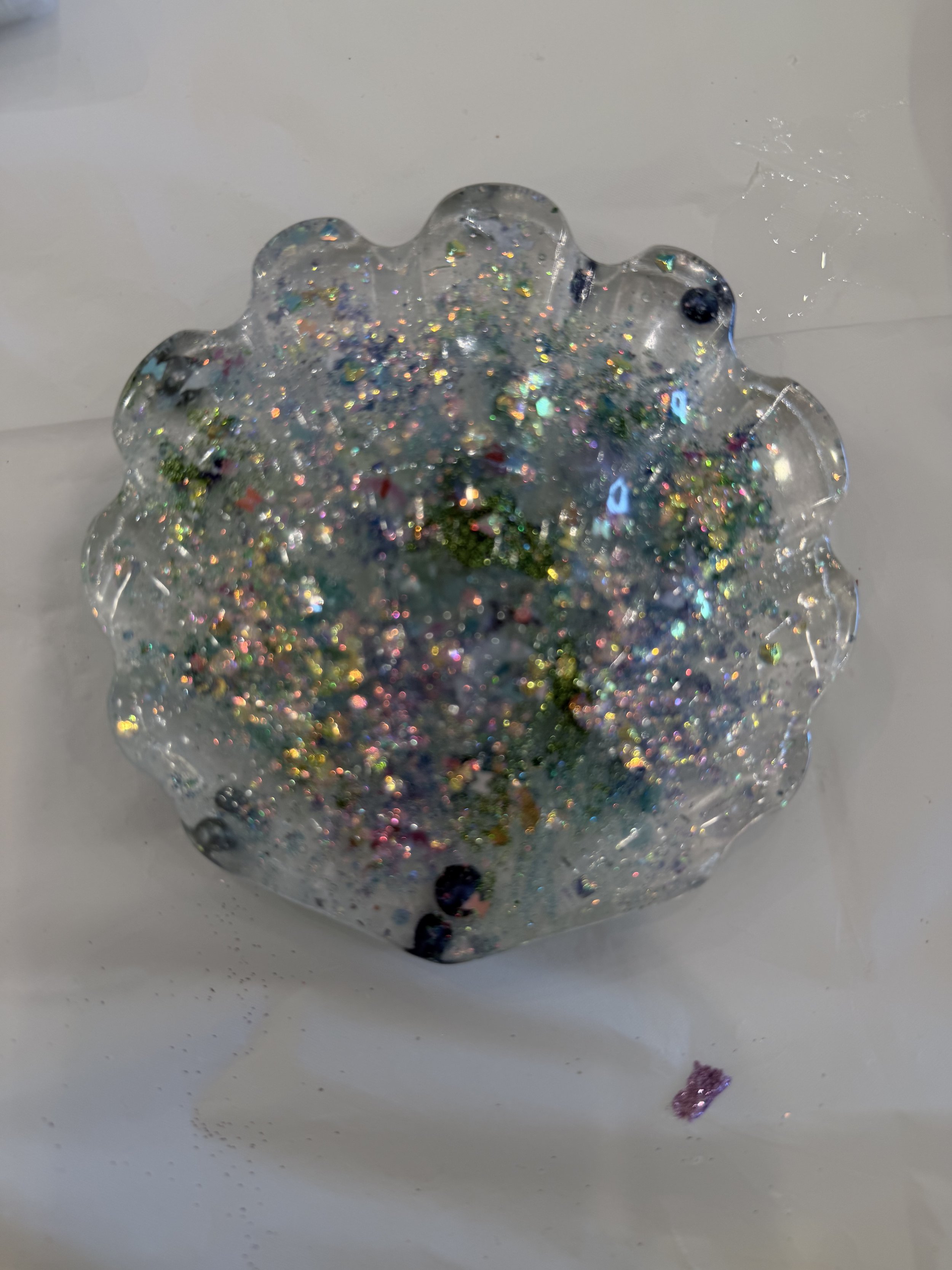 A clear, decorative gel-like ornament with multicolored glitter inside, placed on a white surface.