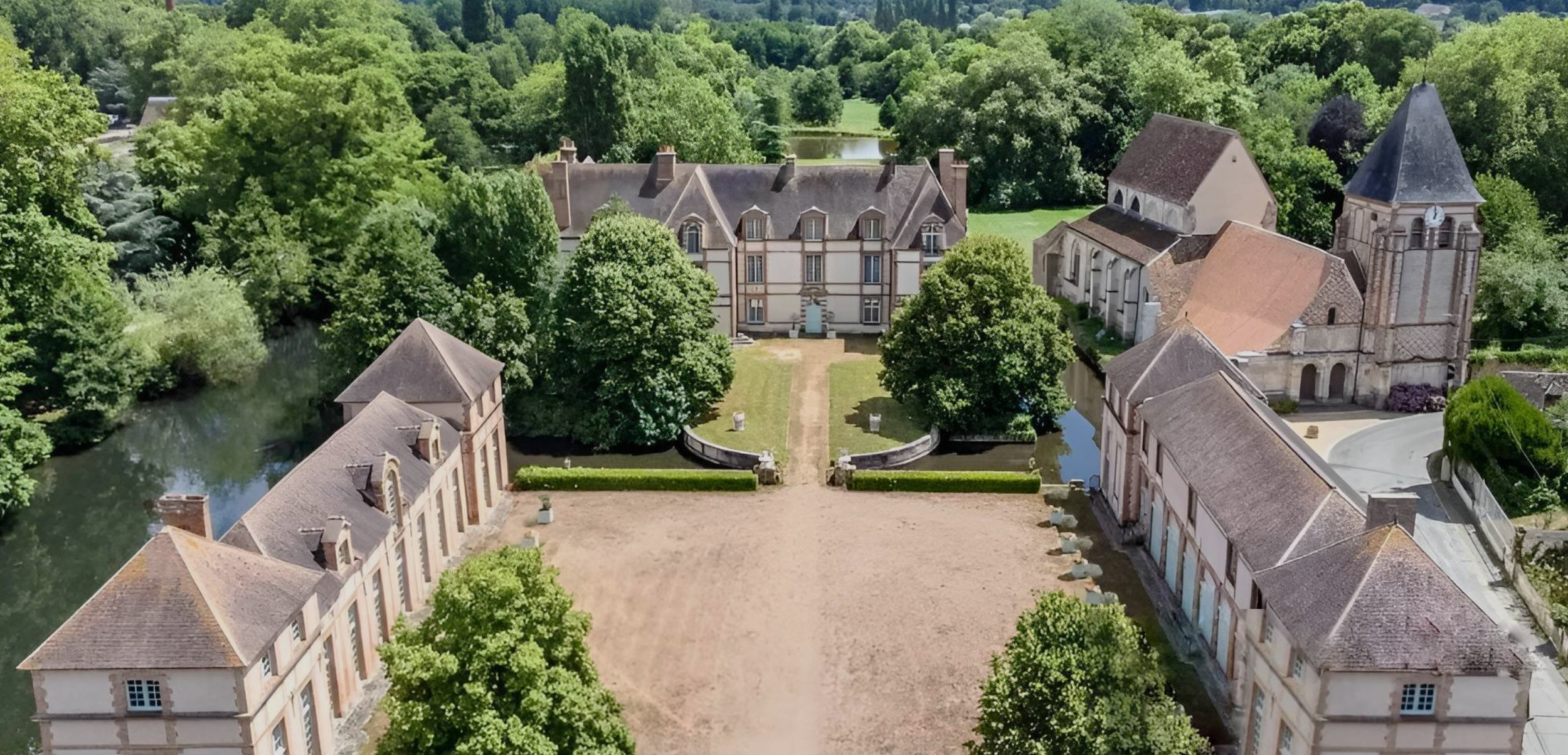 An aerial view of a historic estate with large buildings, surrounded by lush green trees and water features, including ponds and small rivers.